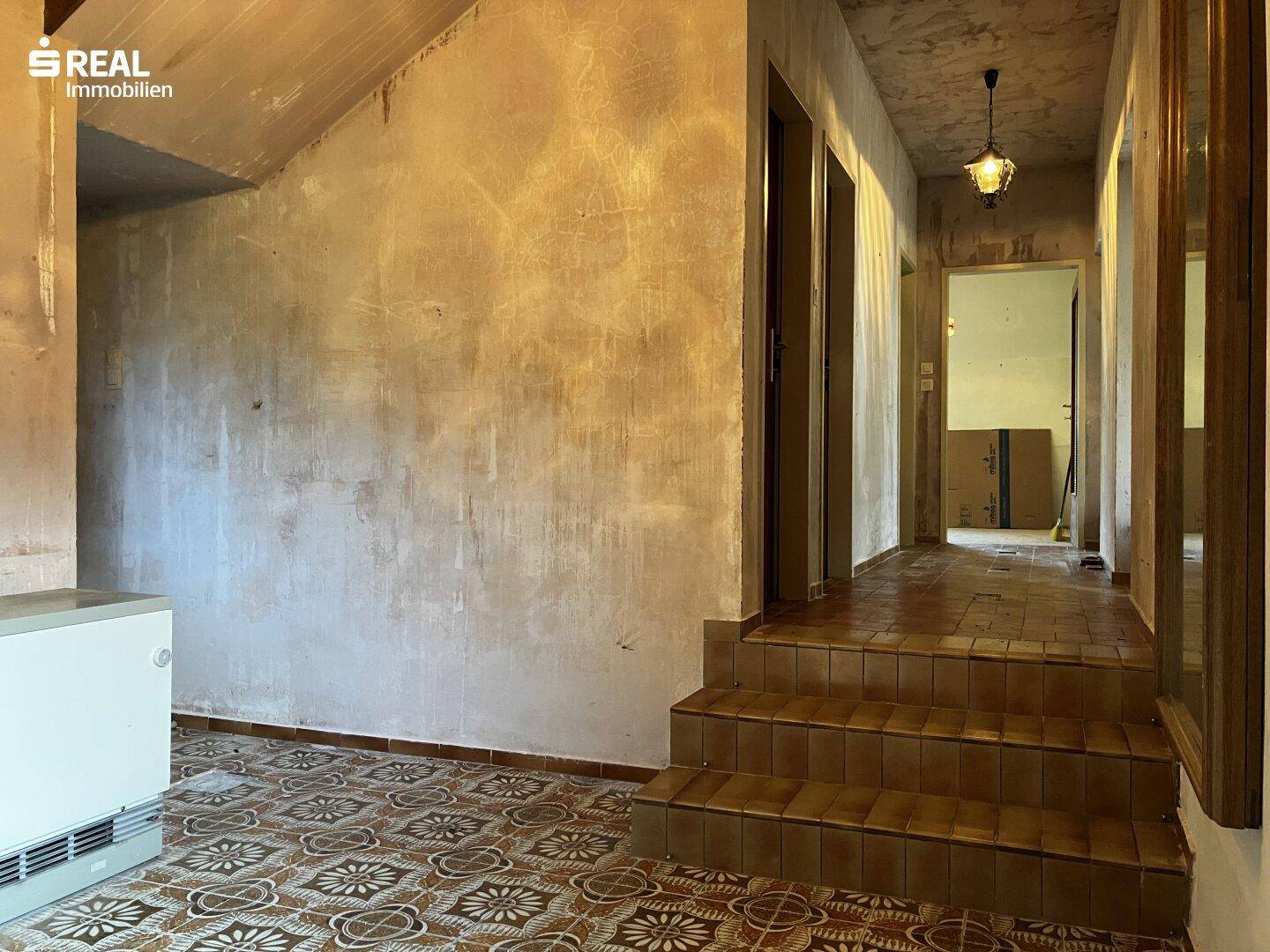 Eingangsbereich mit gefliestem Boden, Treppe und unfertigen Wänden, bereit zur Renovierung.
