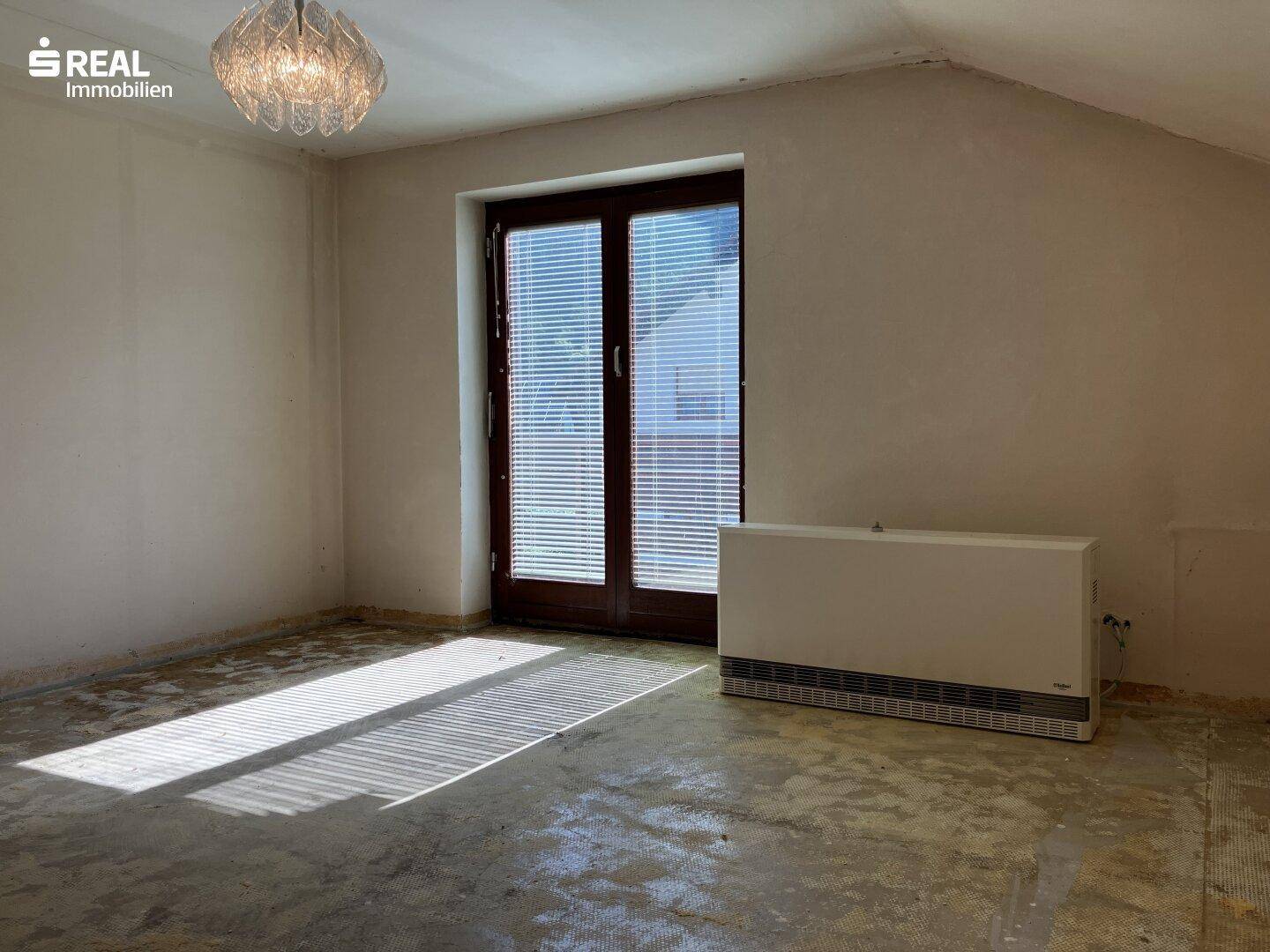 Helles Schlafzimmer mit Balkonzugang und unfertigem Boden, bietet viel Tageslicht.