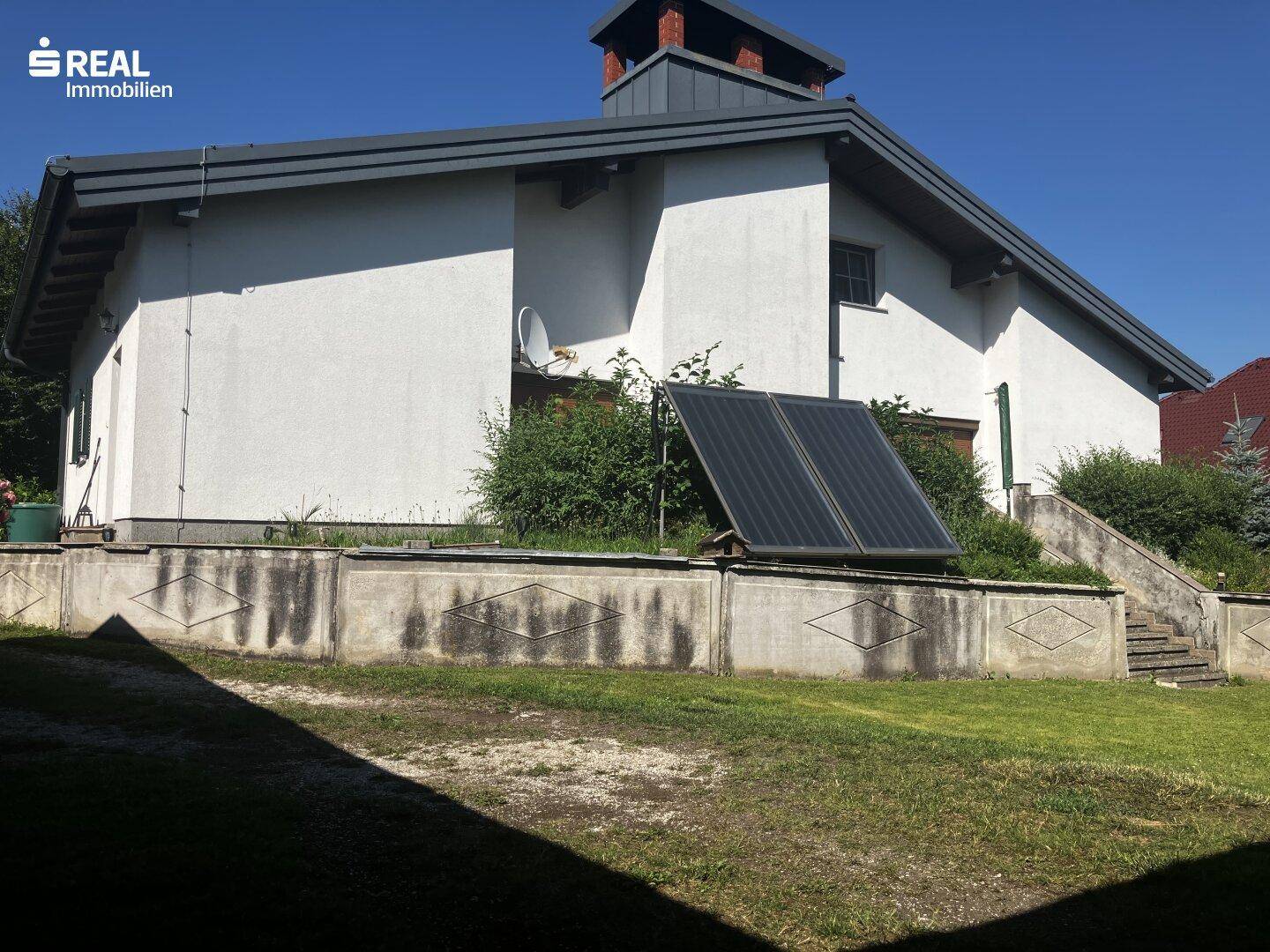 Rückansicht des Hauses mit Solaranlage auf dem Rasen und einer Betonmauer.