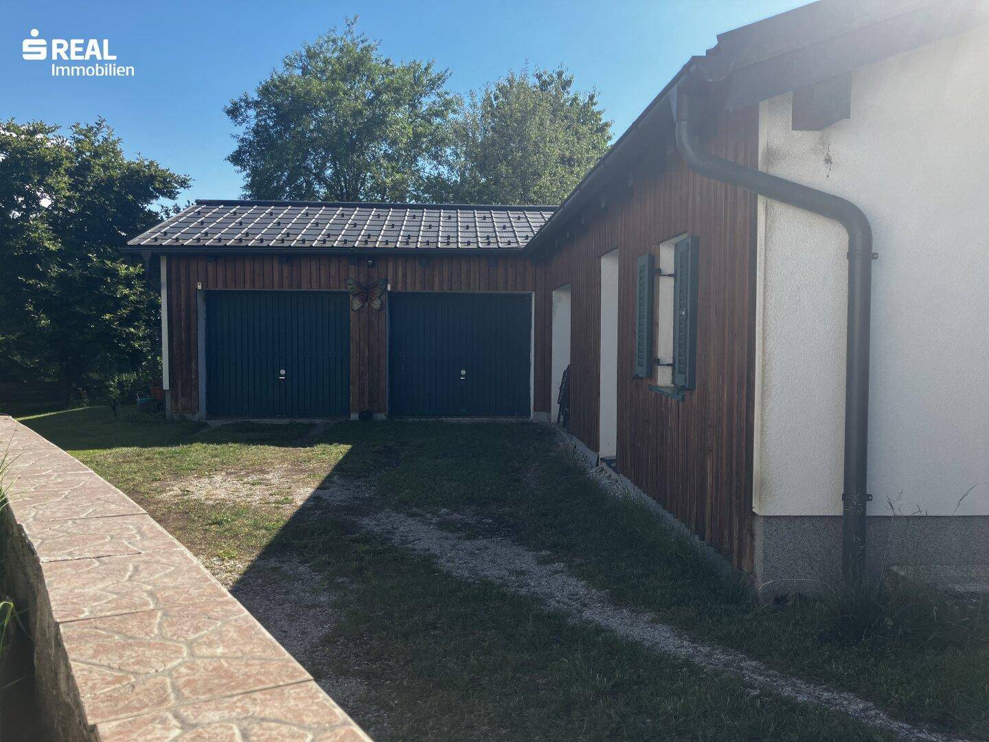 Doppelgarage mit Holzwänden und dunklen Toren neben dem Wohnhaus.