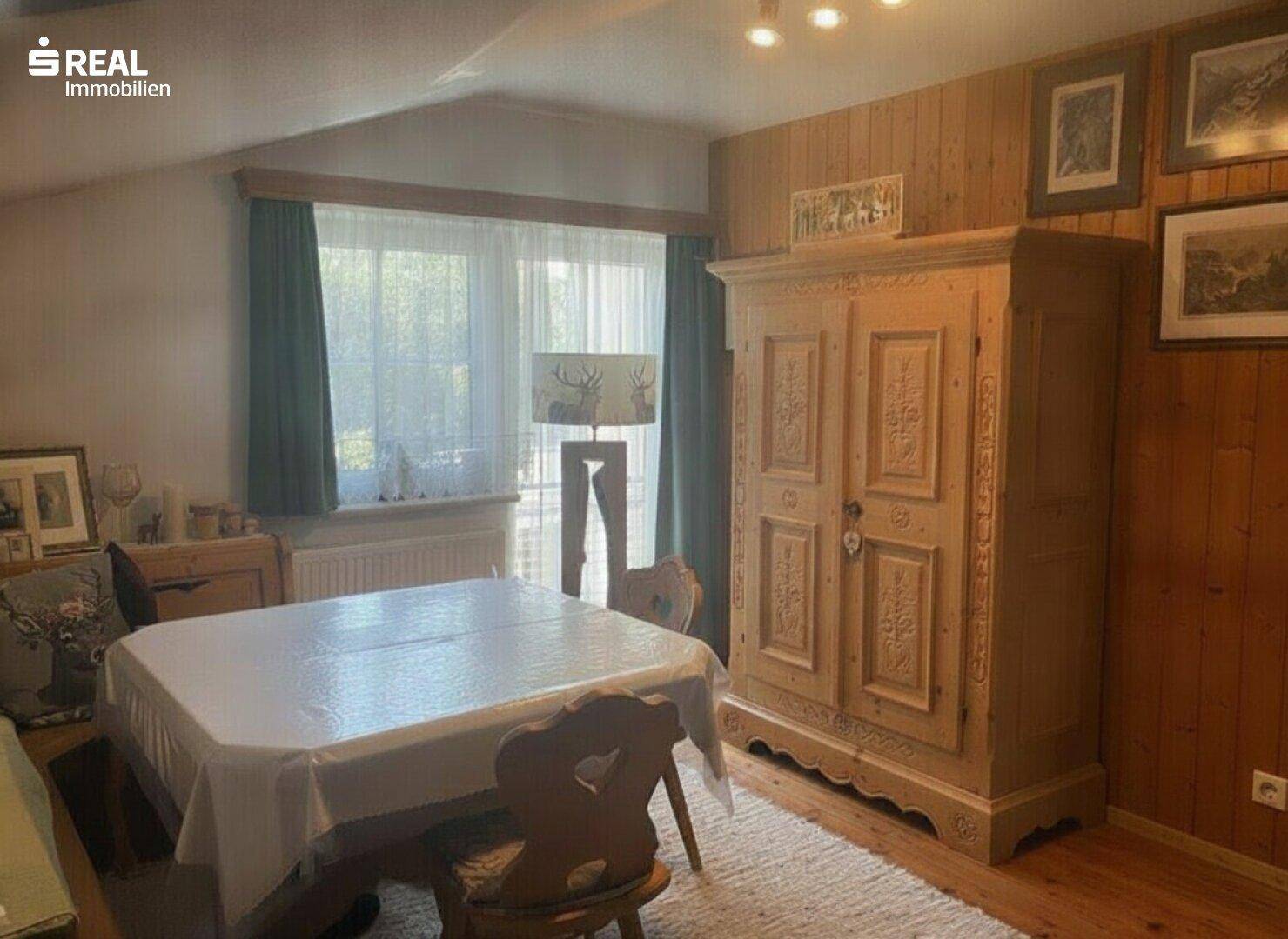 Heller Essbereich mit Holztisch, geschnitztem Schrank und Blick ins Grüne.