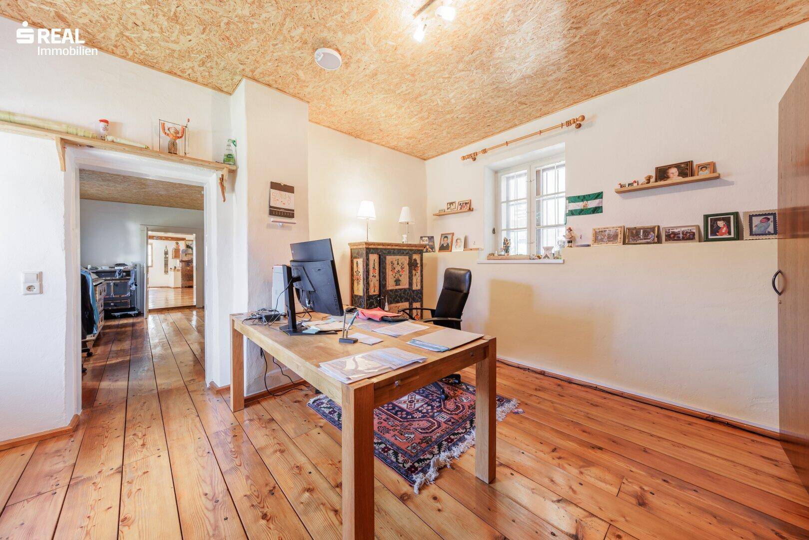 Ruhiges Arbeitszimmer mit Holzdielenboden, Schreibtisch und traditioneller Einrichtung unter Holzdach.