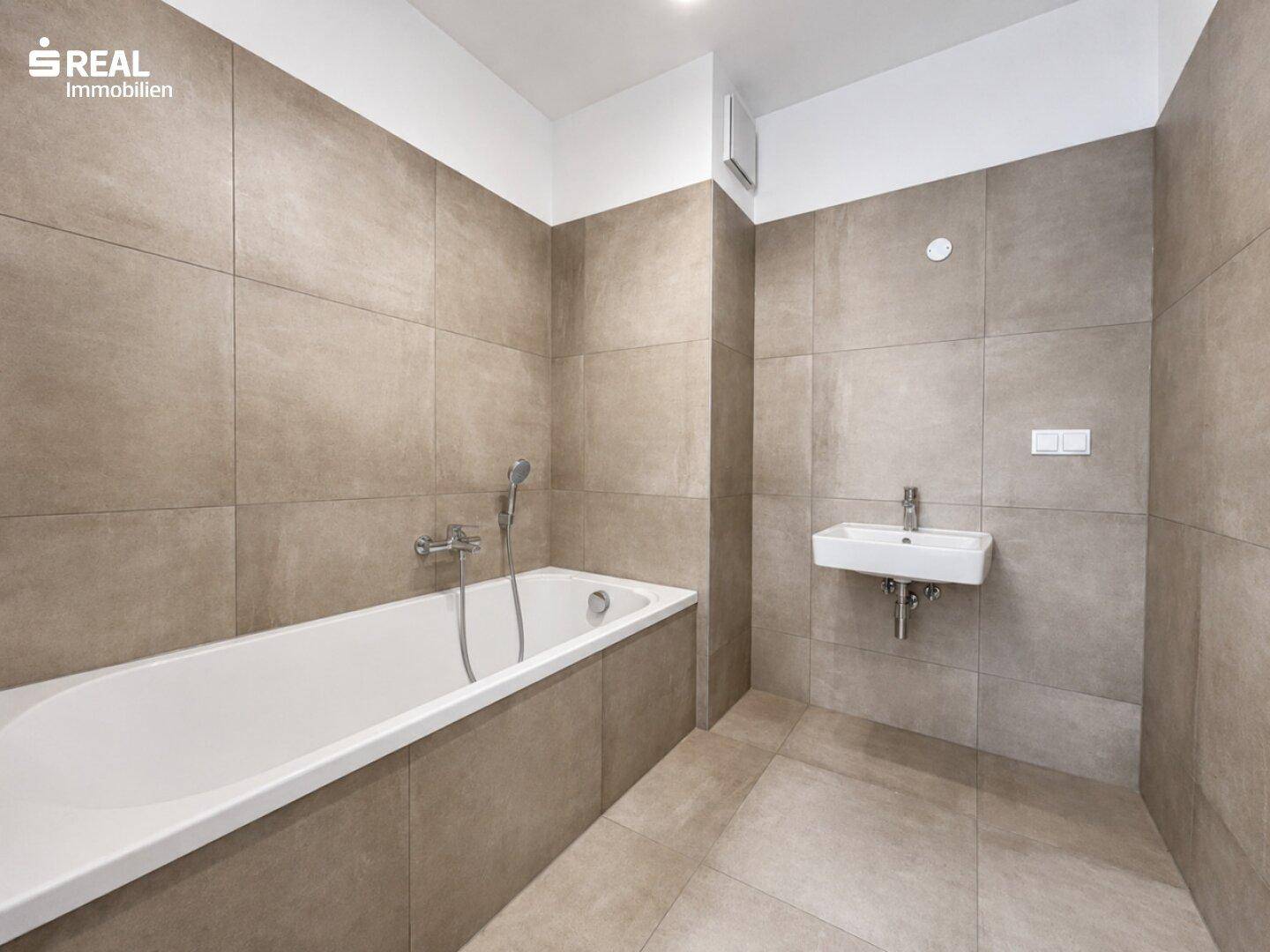 Modernes Badezimmer mit beigefarbenen Fliesen, Badewanne und einem schlichten Waschbecken.