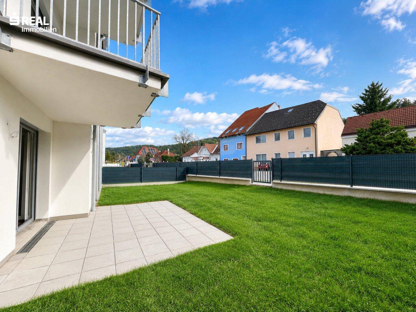 Sonniger Gartenbereich mit Terrasse und Blick auf die umliegende Wohnbebauung.