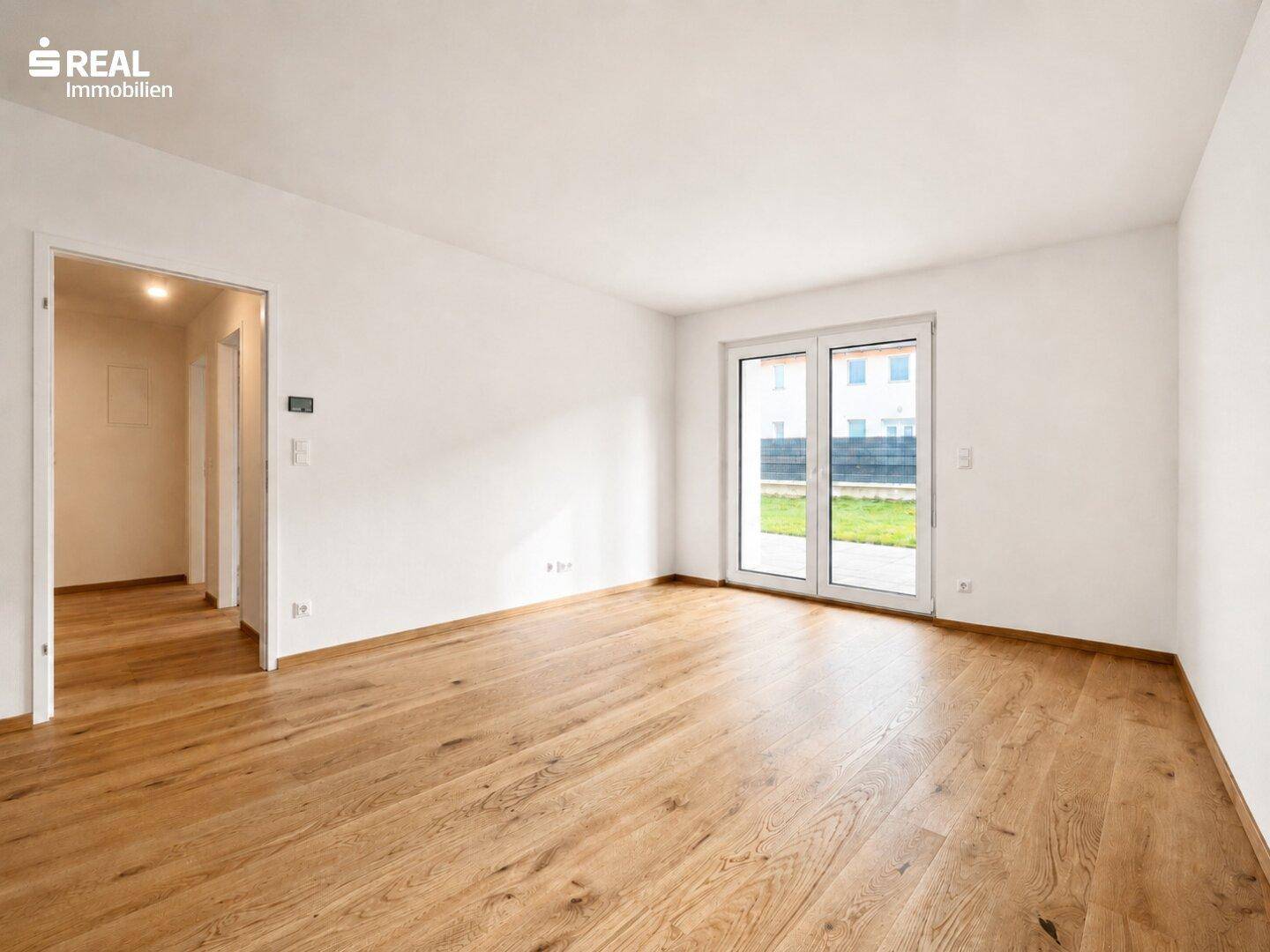 Geräumiges Wohnzimmer mit hellem Holzparkett und direktem Zugang zur Terrasse und Garten.