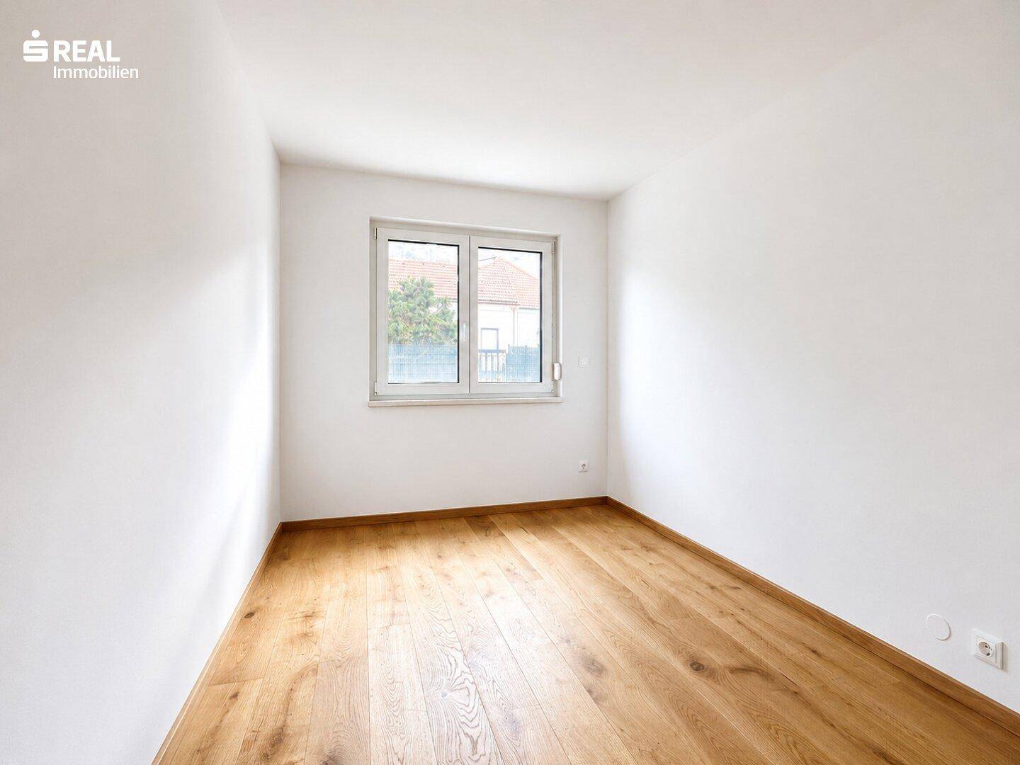Helles Schlafzimmer mit Eichenparkett und einem Fenster, das viel Tageslicht hereinlässt.