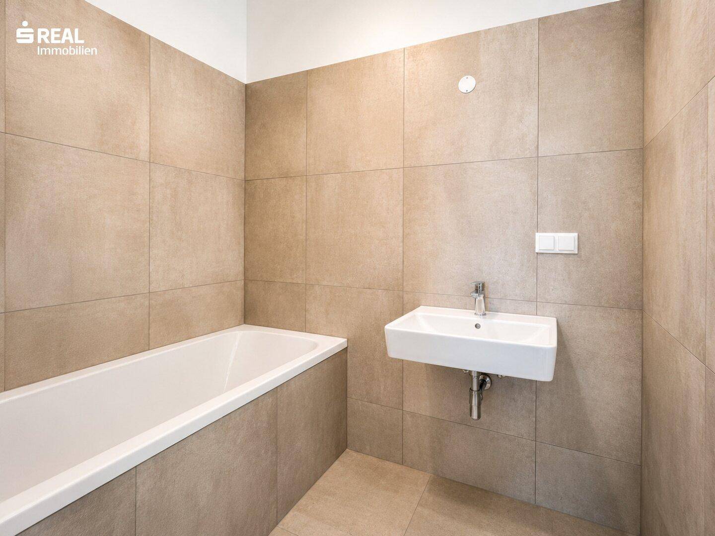 Modernes Badezimmer mit Badewanne, Einzelwaschbecken und beigefarbenen Wand- und Bodenfliesen.