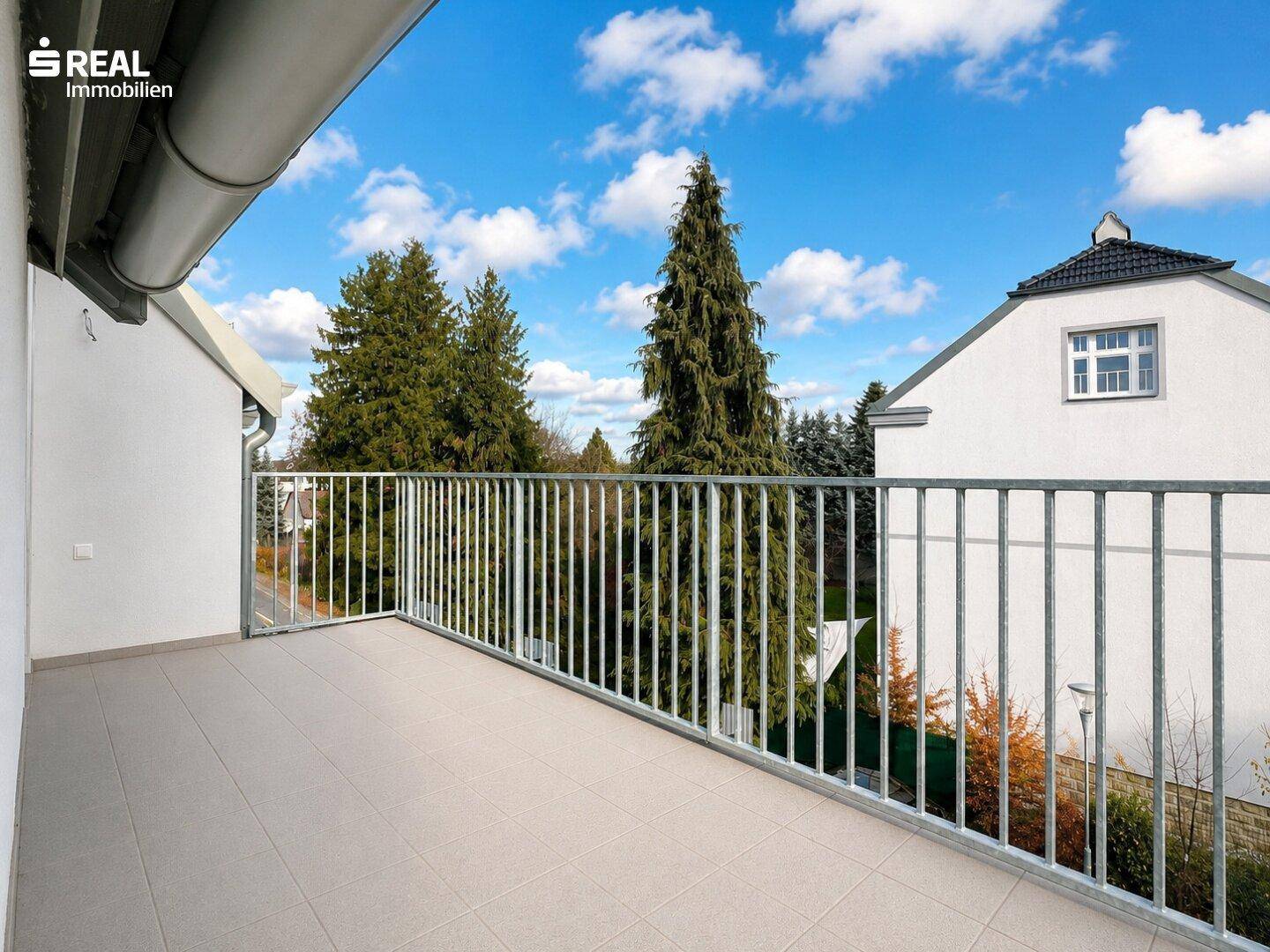 Geräumiger Balkon mit Fliesenboden und Blick auf die umliegende Wohngegend und Bäume.