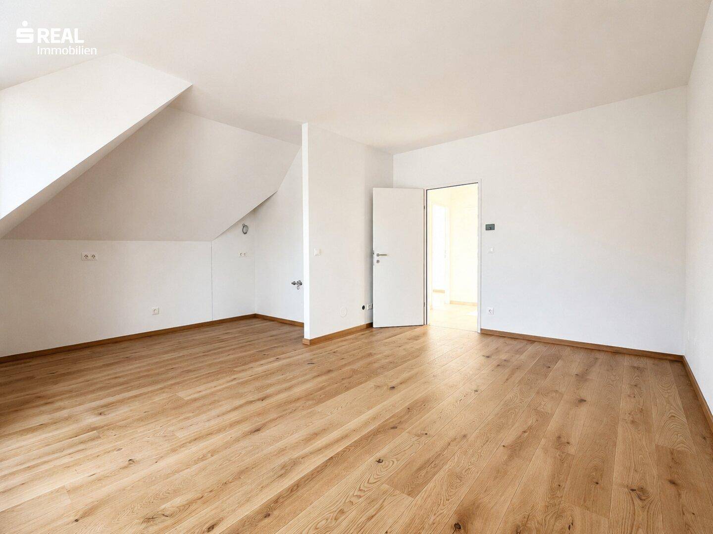 Leeres Zimmer im Dachgeschoss mit Holzboden und schrägen Wänden, bereit zur individuellen Gestaltung.