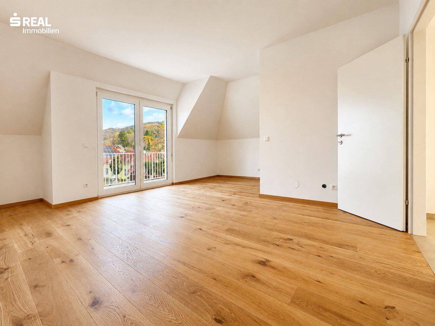 Helles Zimmer im Dachgeschoss mit Holzboden und Zugang zu einem französischen Balkon.