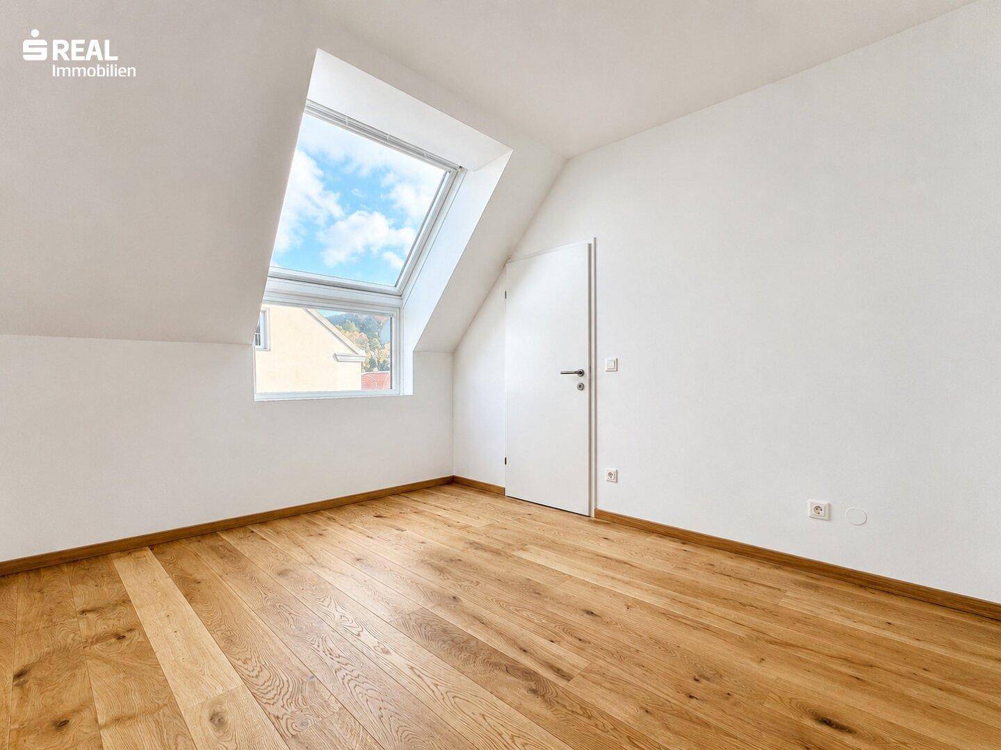 Freundliches Zimmer im Dachgeschoss mit Holzboden und großem Dachfenster für viel Licht.