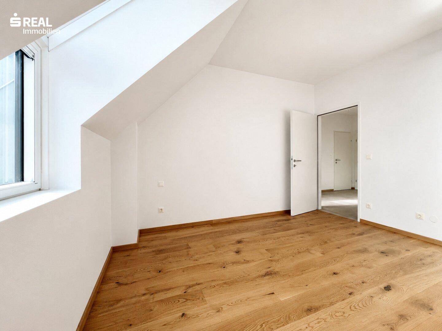 Helles Zimmer mit Holzboden und schrägen Wänden im Dachgeschoss, ideal als Schlaf- oder Arbeitszimmer.