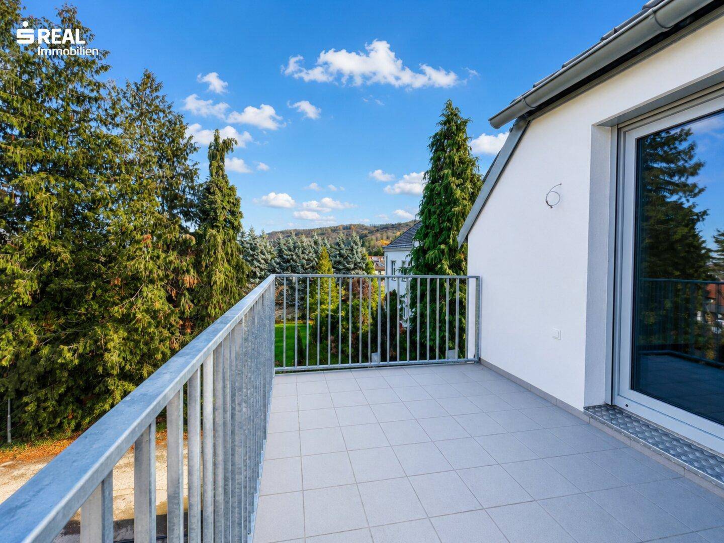 Heller Balkon mit Fliesen und Metallgeländer, bietet einen schönen Ausblick auf die bewaldete Umgebung.