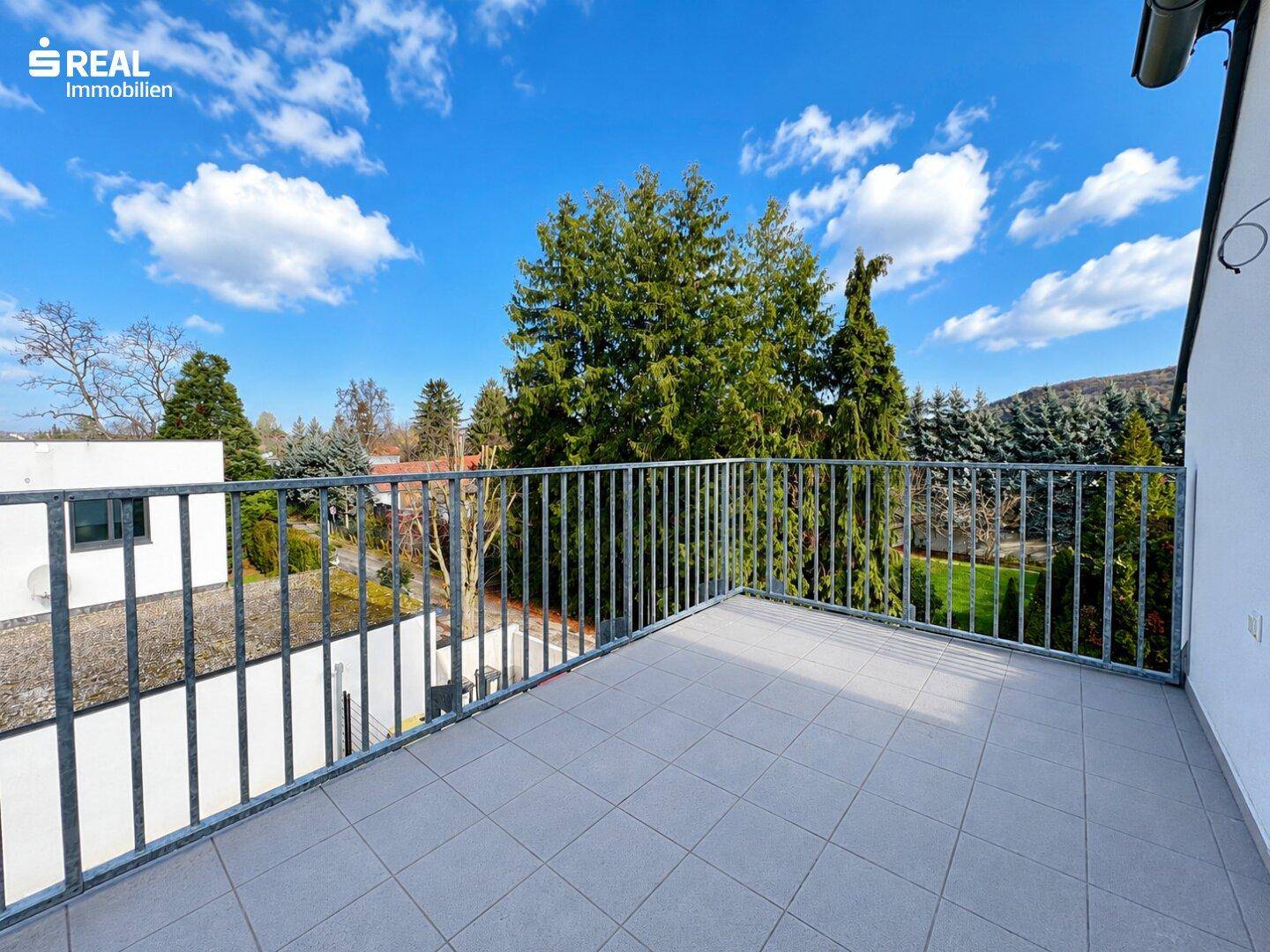 Heller Balkon mit Fliesenboden und Metallgeländer, bietet einen Ausblick auf die grüne Umgebung.