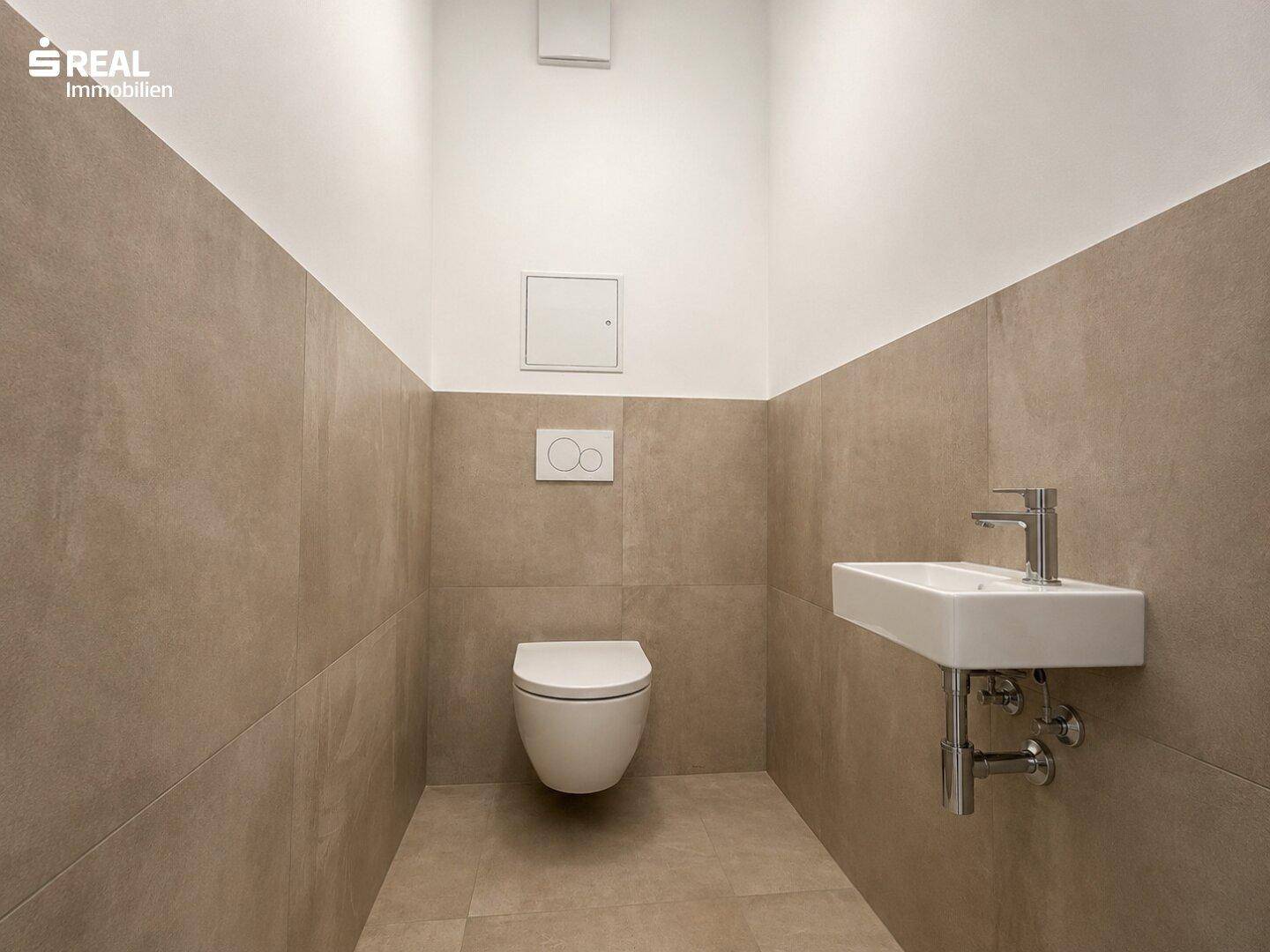 Modernes Gäste-WC mit beigefarbenen Fliesen, wandhängendem WC und kleinem Waschbecken.