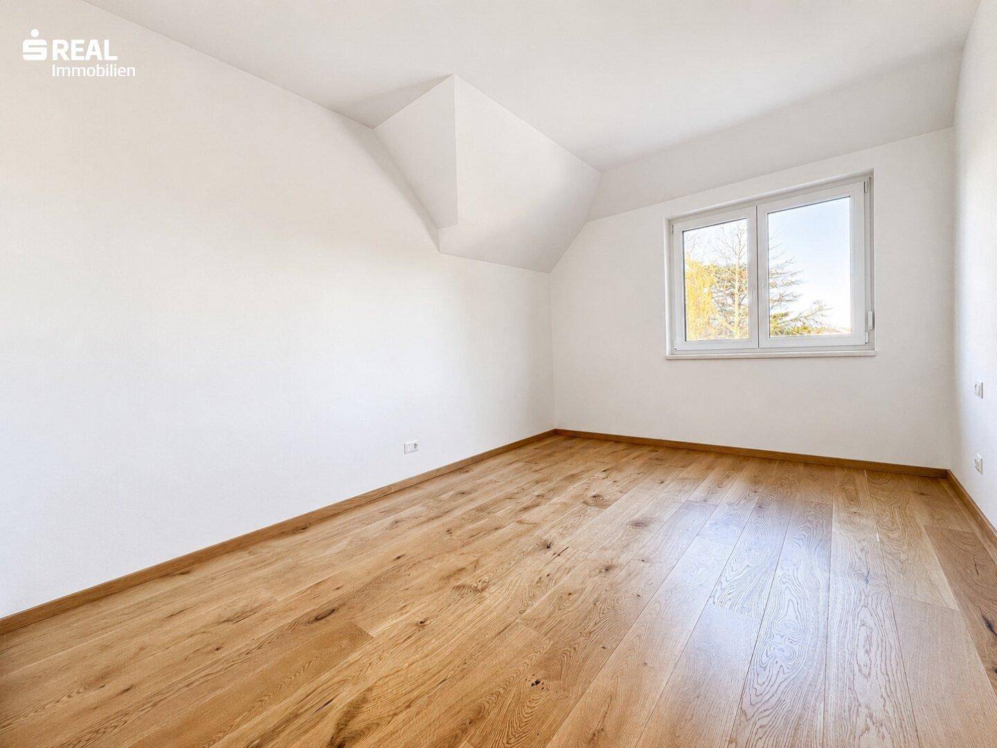 Helles Zimmer mit Holzboden und Dachschräge, bietet viel natürliches Licht durch das Fenster.
