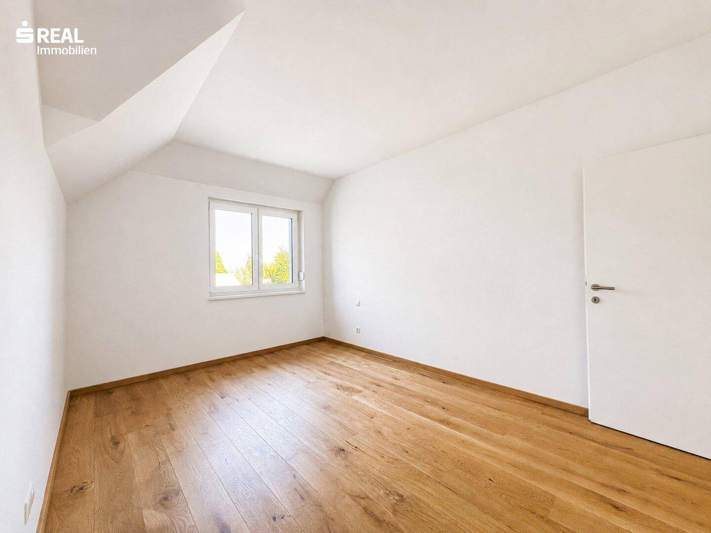 Helles Zimmer mit Holzboden und Dachschräge, bietet viel natürliches Licht durch das Fenster.