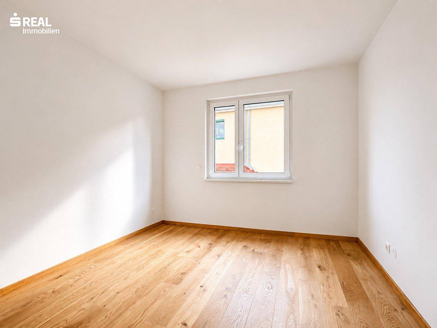 Ruhiges Zimmer mit Eichenparkett und einem Fenster, das viel Tageslicht hereinlässt.
