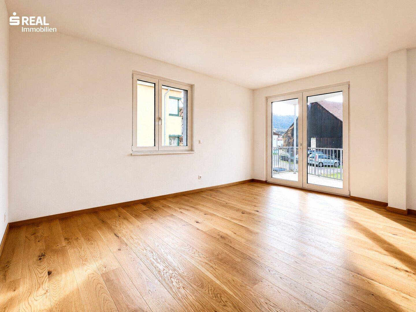 Heller Wohnbereich mit Holzboden und Balkonzugang, der viel natürliches Licht bietet.