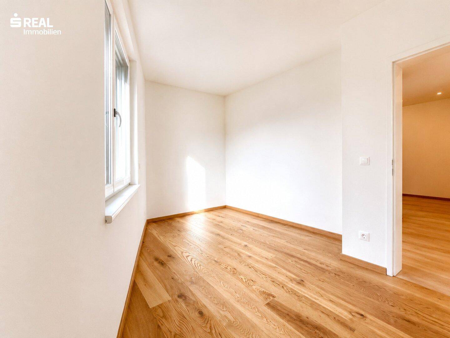 Sonniger Raum mit Holzboden und großem Fenster, ideal für ein Schlaf- oder Kinderzimmer.