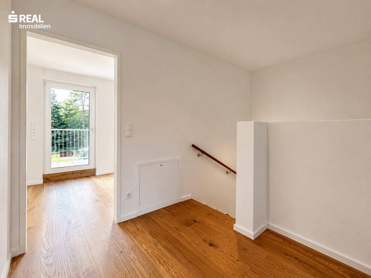 Heller Flur mit Holztreppe und Zugang zu einem Zimmer mit Balkon, ausgestattet mit Holzboden.