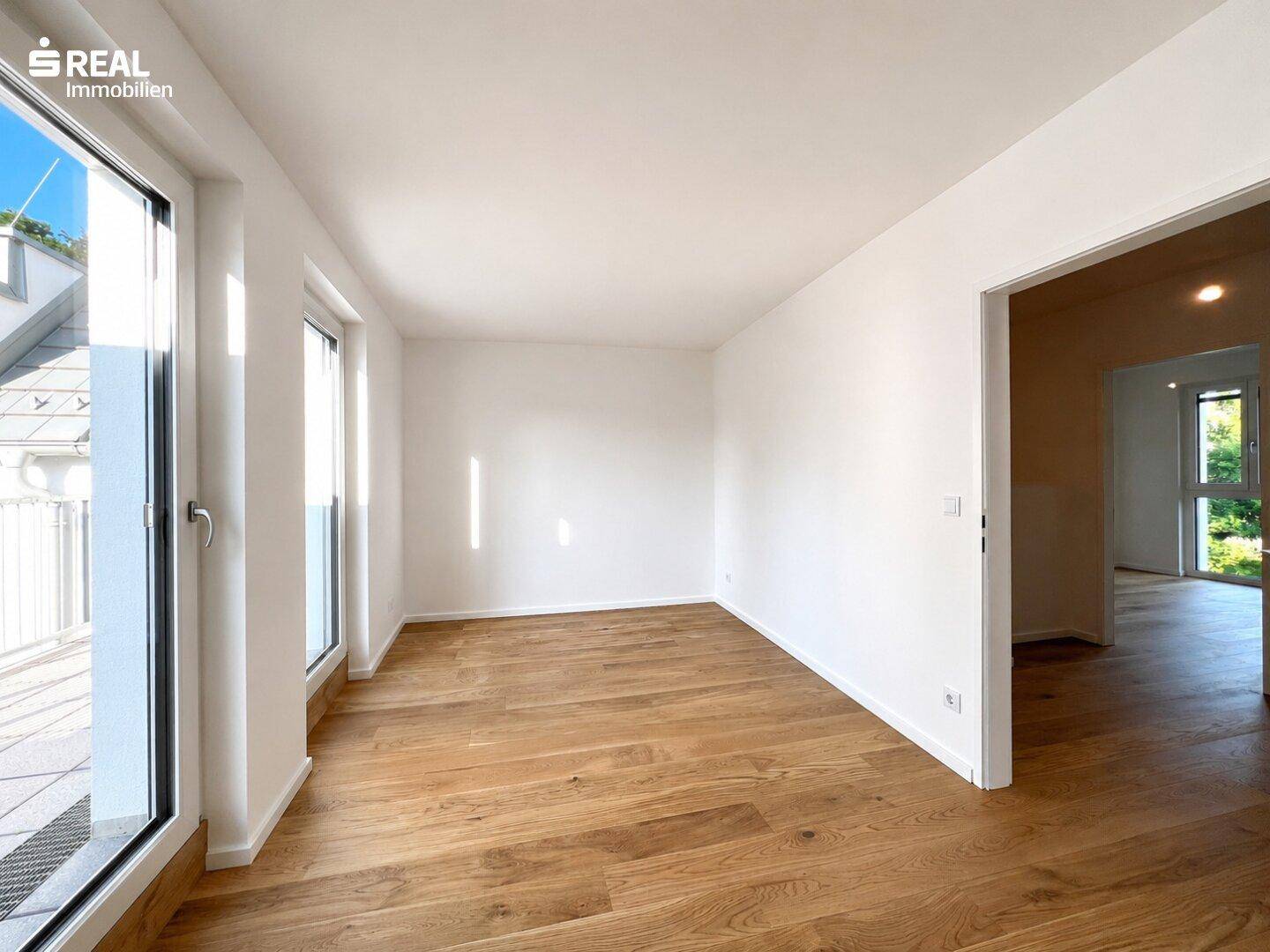 Geräumiges, helles Wohnzimmer mit großen Fenstern und Zugang zur Terrasse, ausgestattet mit Holzboden.