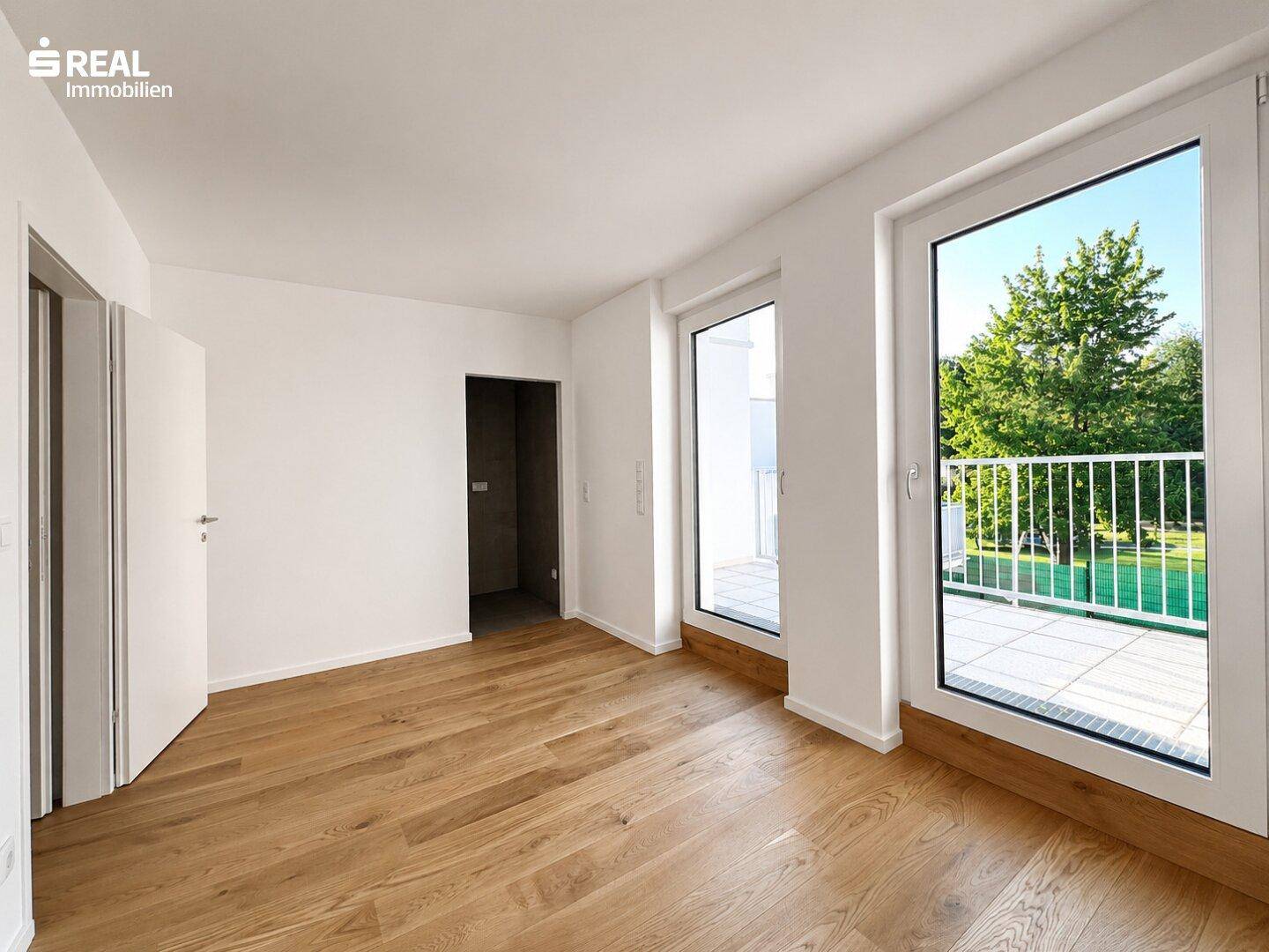 Helles Schlafzimmer mit Holzboden und großen Fenstern, die Zugang zu einem Balkon oder einer Terrasse bieten.