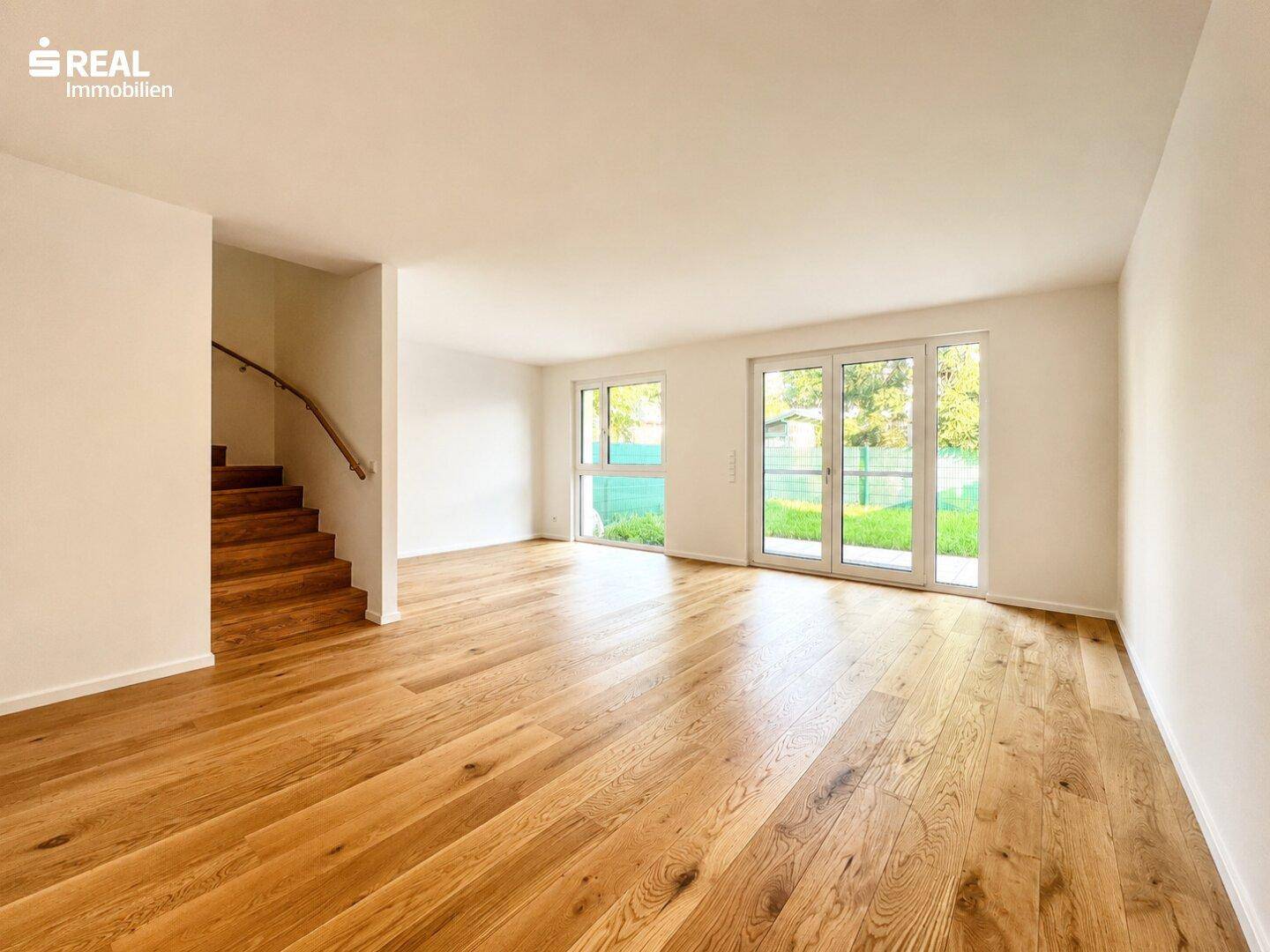 Großzügiger Wohnbereich mit Holzboden, viel Tageslicht und einer offenen Holztreppe.