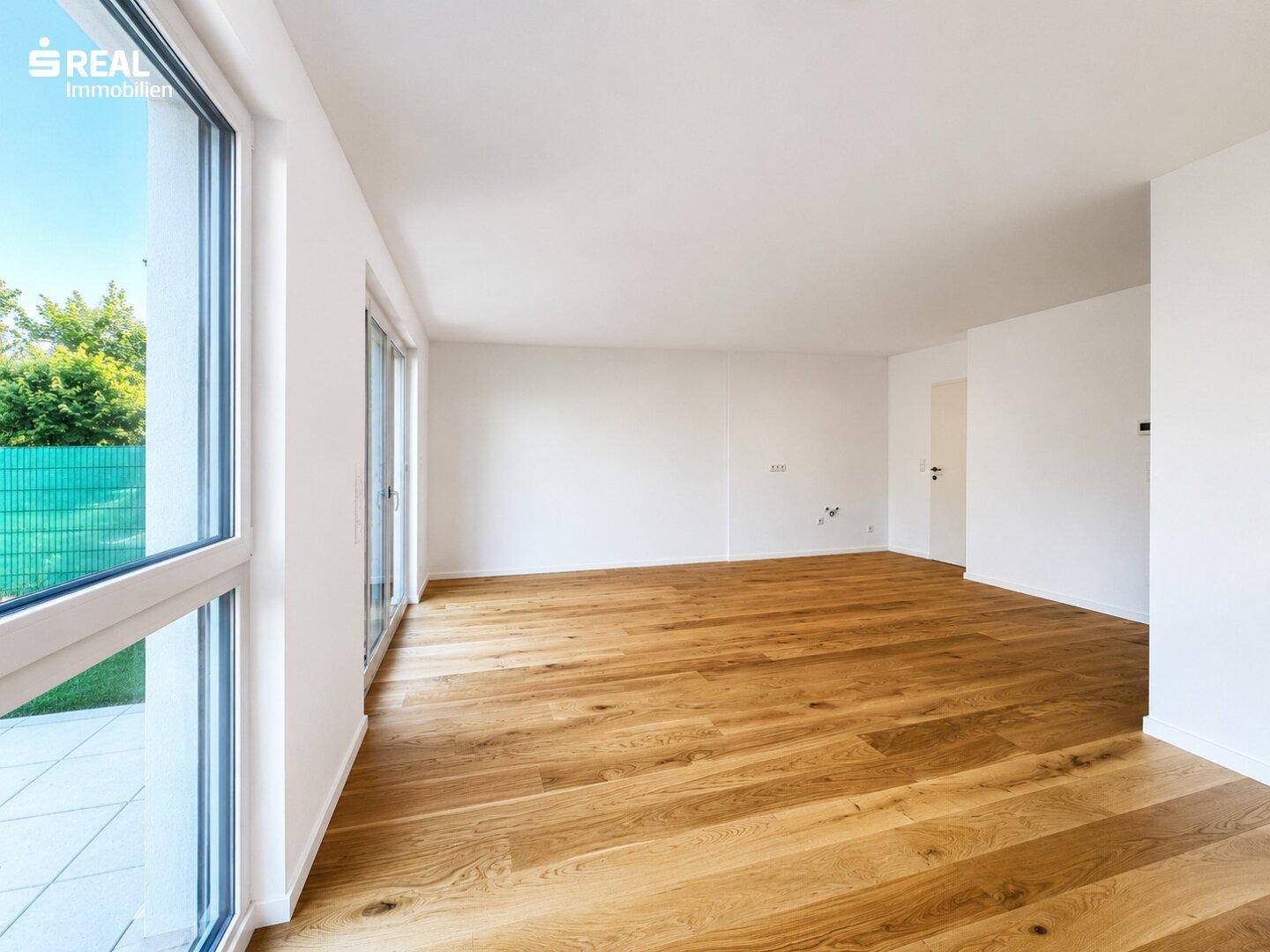 Heller Wohnraum mit Holzboden und großen Fenstern, die viel Tageslicht hereinlassen und Zugang zur Terrasse bieten.