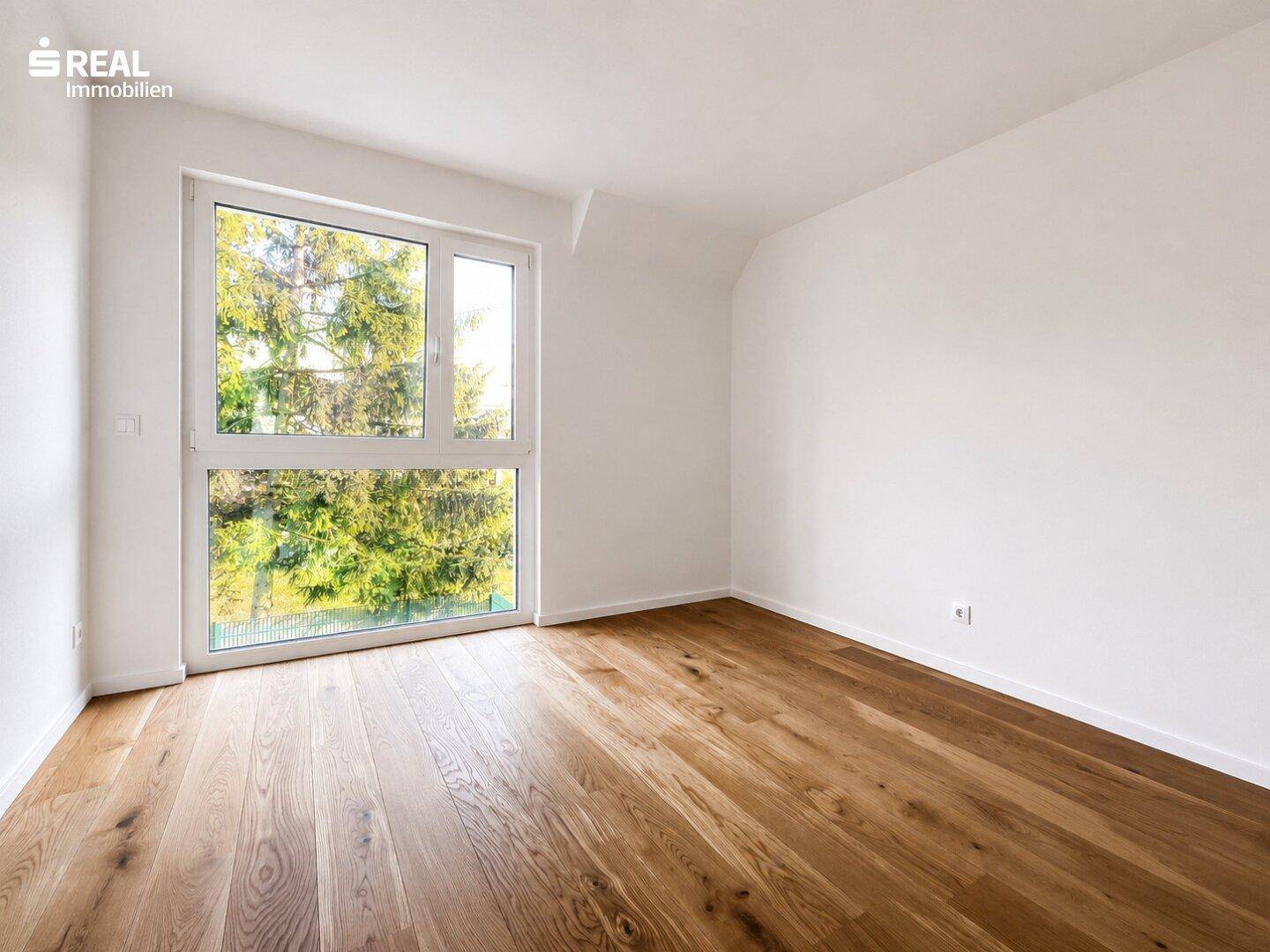 Helles Schlafzimmer mit Holzboden und großem Fenster, das einen schönen Blick ins Grüne bietet.