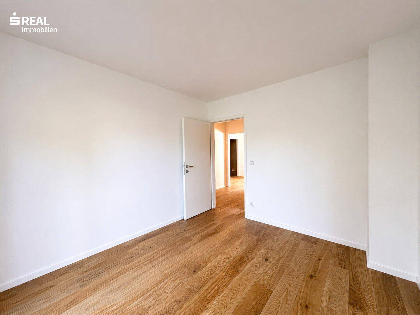 Geräumiges, helles Zimmer mit Holzboden und weiß gestrichenen Wänden, bereit zur individuellen Gestaltung.