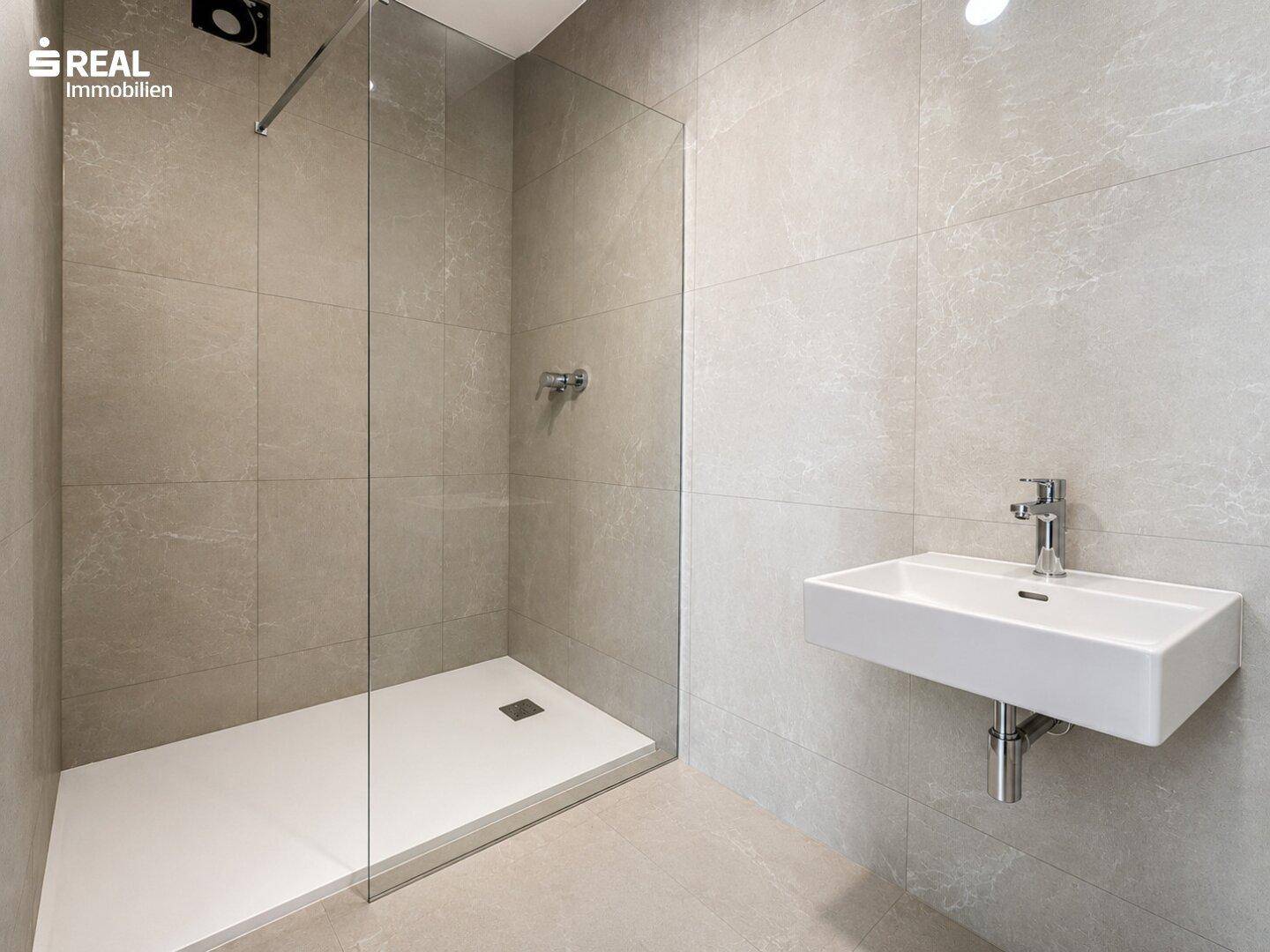 Modernes Badezimmer mit begehbarer Dusche, Wandwaschbecken und großen grauen Fliesen.