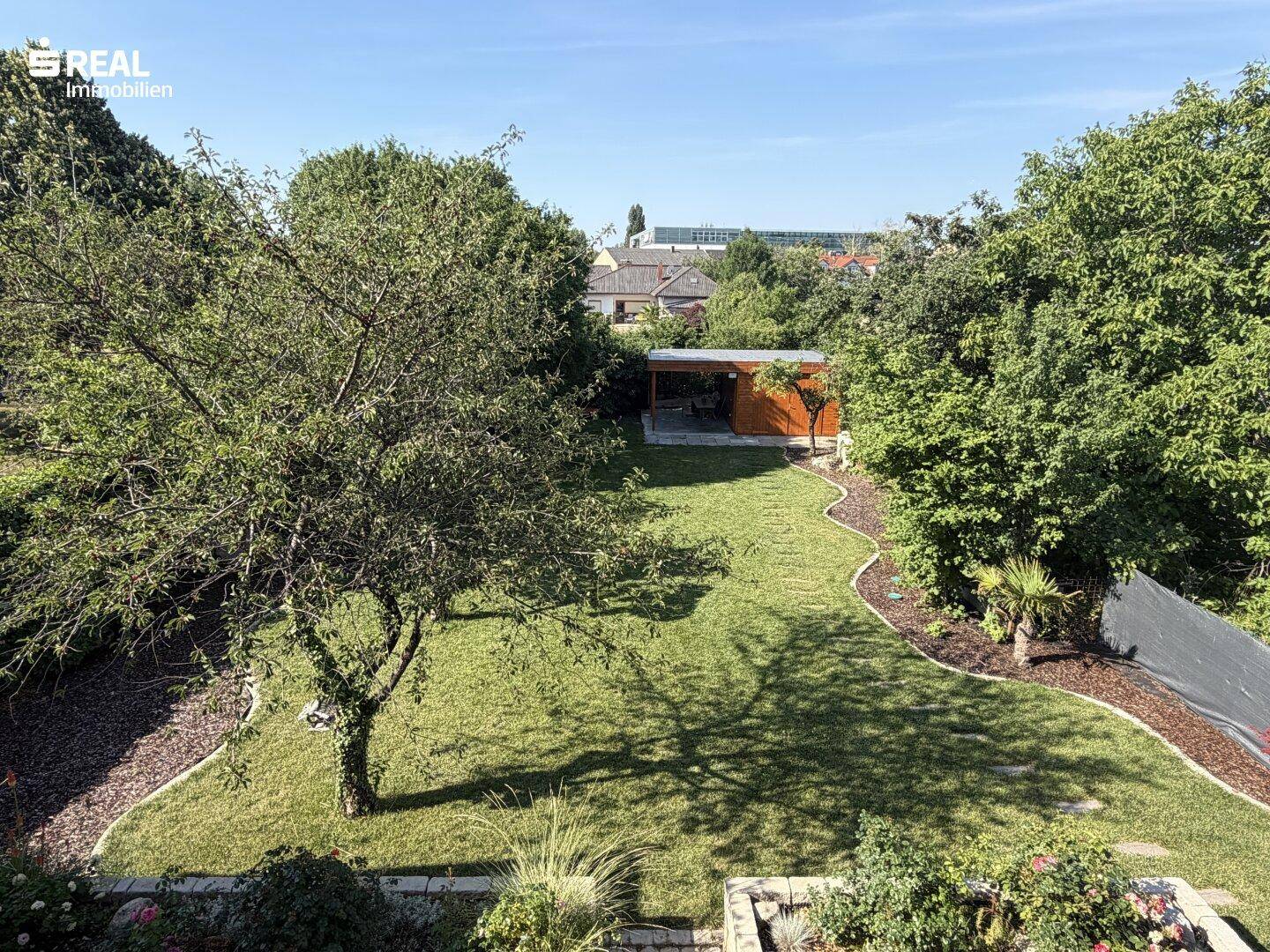 Weitläufiger, gepflegter Garten mit Rasenflächen, Bäumen und einem Gartenhaus im Hintergrund.