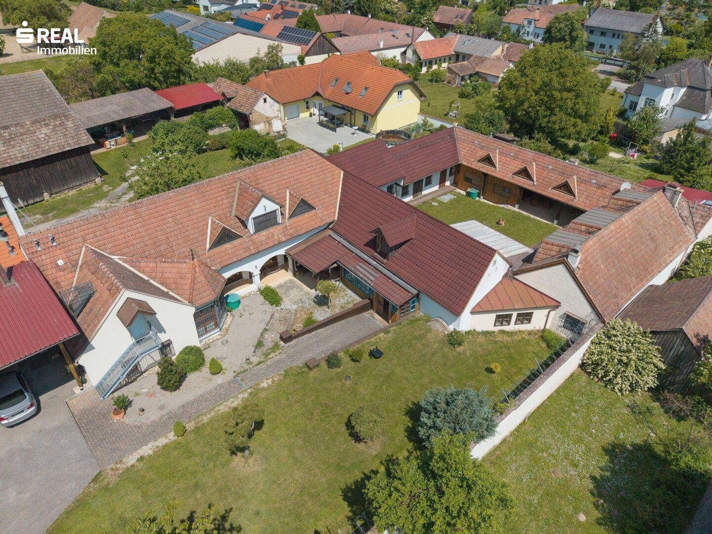 Luftaufnahme des weitläufigen Anwesens mit mehreren Gebäuden, Innenhof und umliegender ländlicher Bebauung.