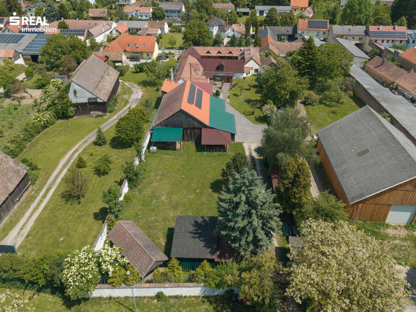 Vogelperspektive des Anwesens mit angrenzenden Feldern, Bäumen und Photovoltaikanlage auf einem Nebengebäude.