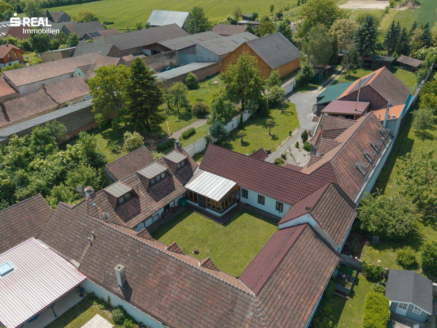 Luftaufnahme des Anwesens mit großem Innenhof, umgeben von Gebäudeteilen und roten Ziegeldächern.