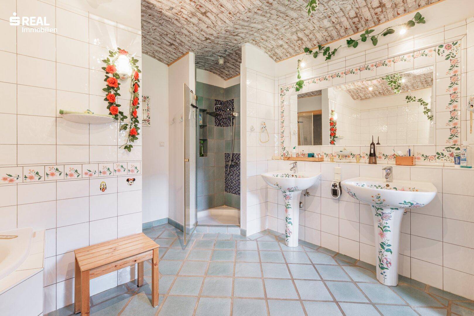 Geräumiges Badezimmer mit zwei Waschbecken, Dusche, Fliesenboden und dekorativer Decke.