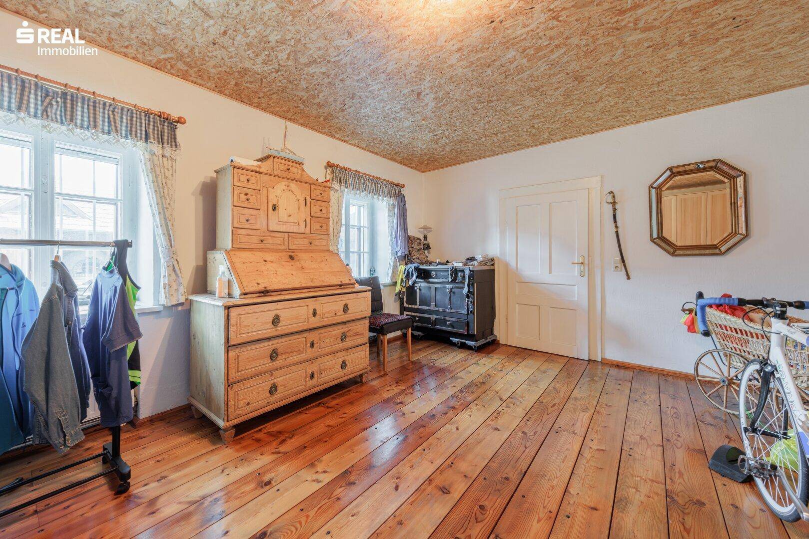 Helles Schlafzimmer mit Holzdielenboden, traditionellen Möbeln und Fenstern mit Blick ins Grüne.