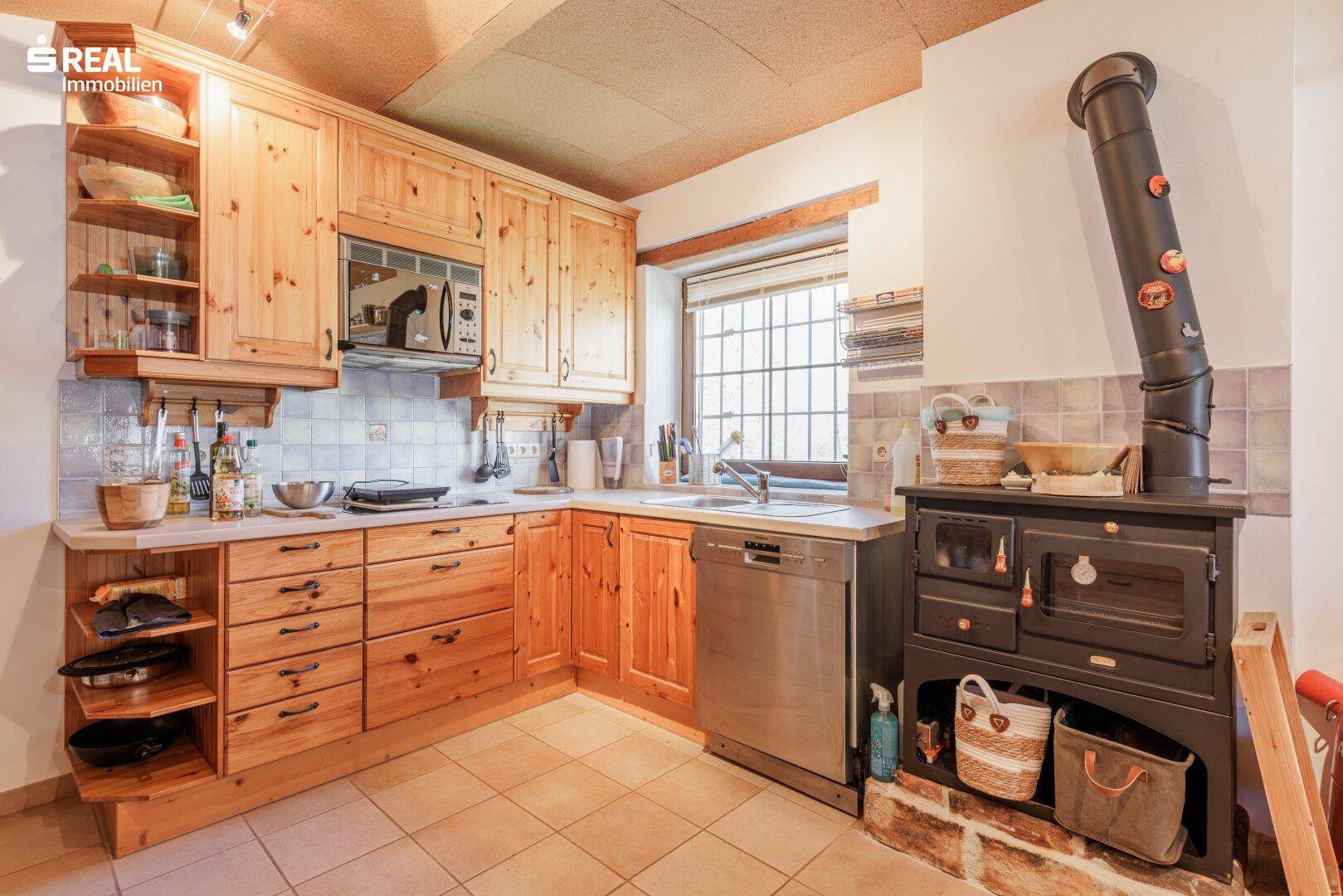 Traditionelle Küche mit Holzschränken, Spülmaschine, Fenster und einem rustikalen Holzofen.