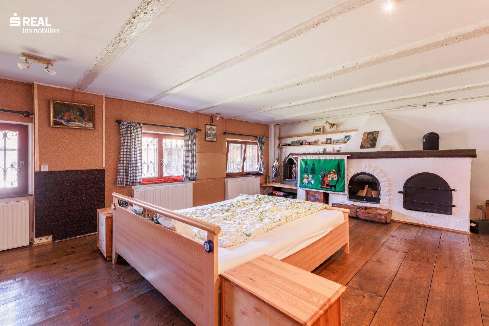 Gemütliches Schlafzimmer mit Holzdielenboden, Doppelbett und einem traditionellen Kamin mit Sitzbank.