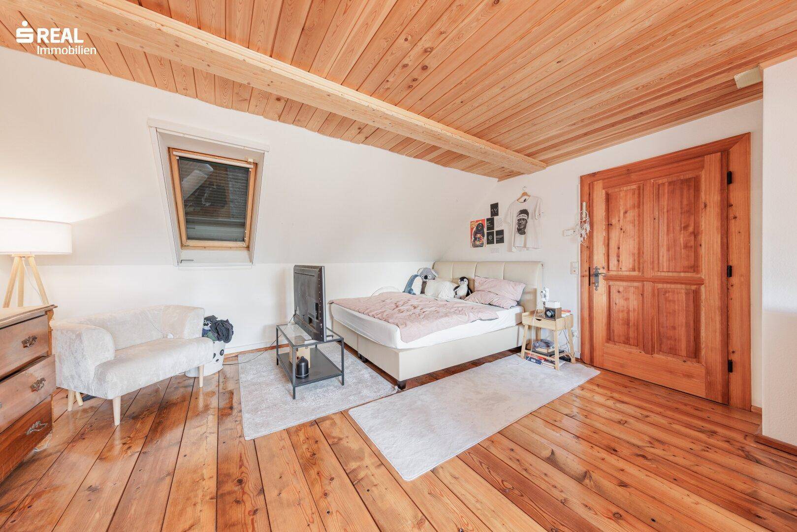 Helles Schlafzimmer im Dachgeschoss mit Holzdielenboden, Dachfenster und Holzbalkendecke.