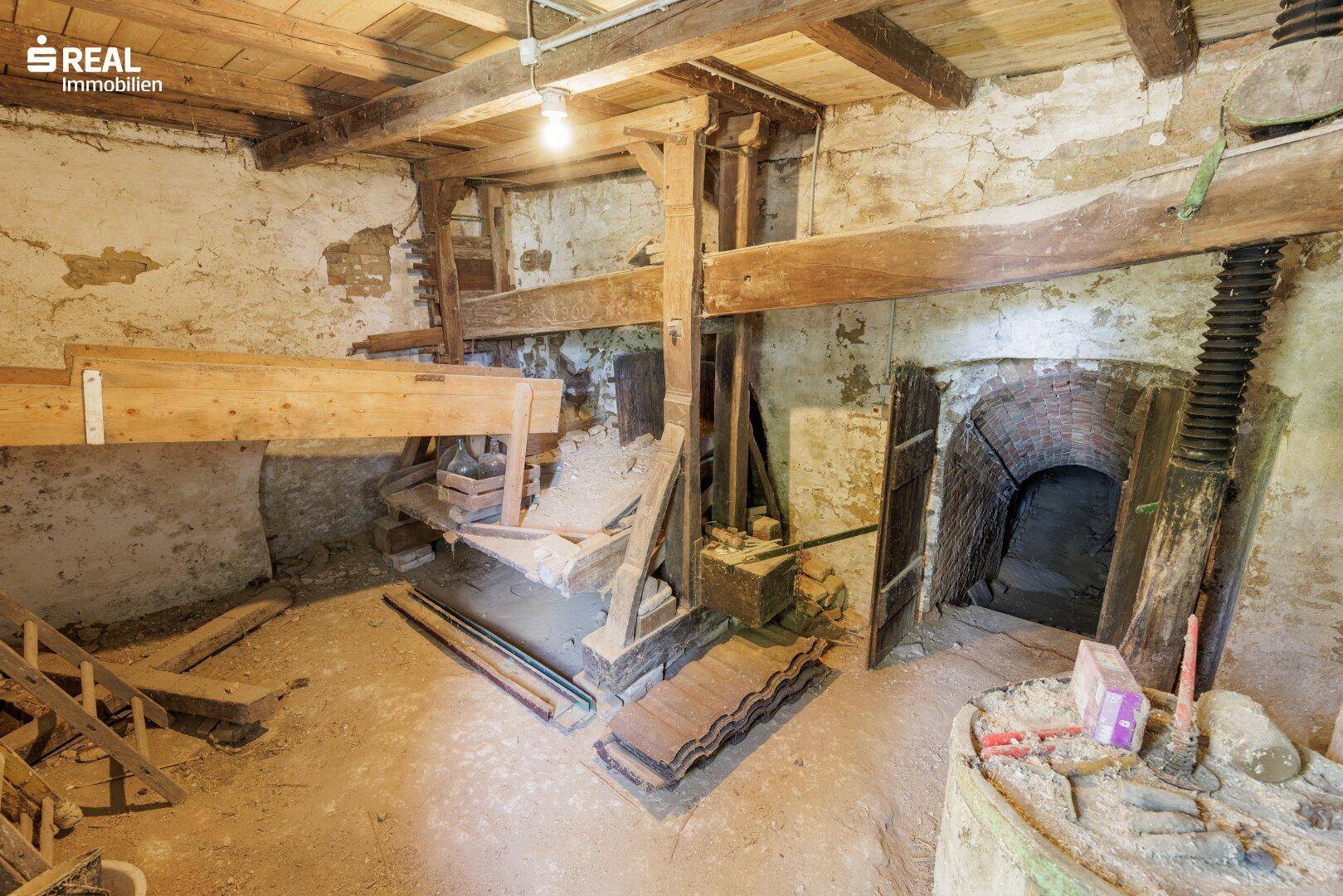 Historischer Kellerraum mit freiliegenden Steinmauern, Holzbalken und einem gemauerten Bogen.