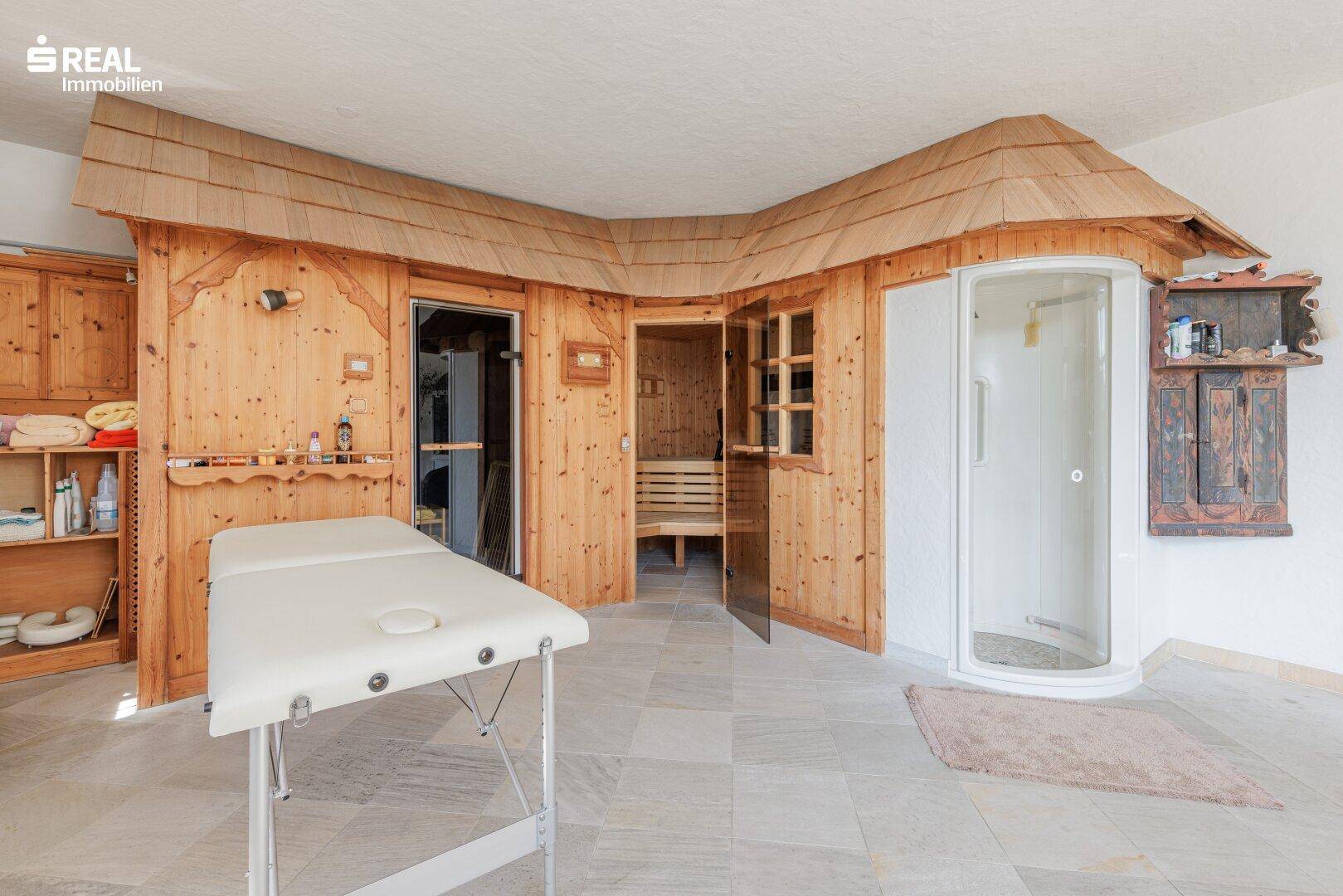Wellnessbereich mit Holzvertäfelung, Sauna, Duschkabine und einer Massageliege.