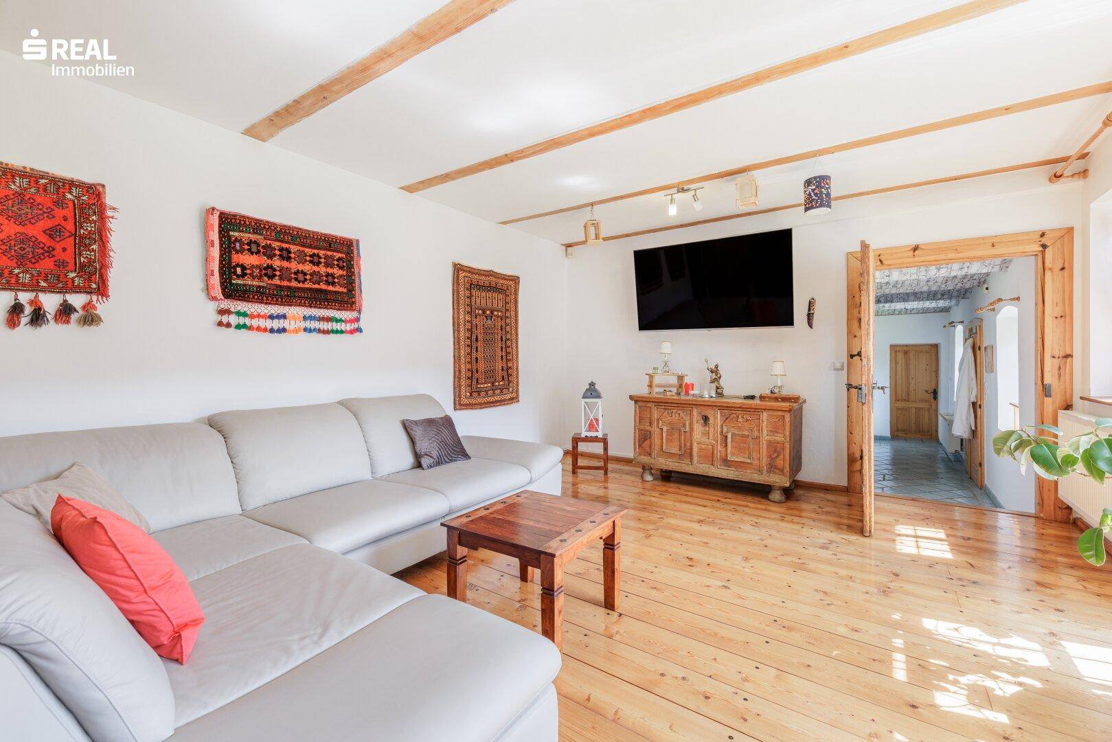 Gemütliches Wohnzimmer mit Holzdielenboden, bequemer Couch, traditionellen Teppichen und Holzbalkendecke.