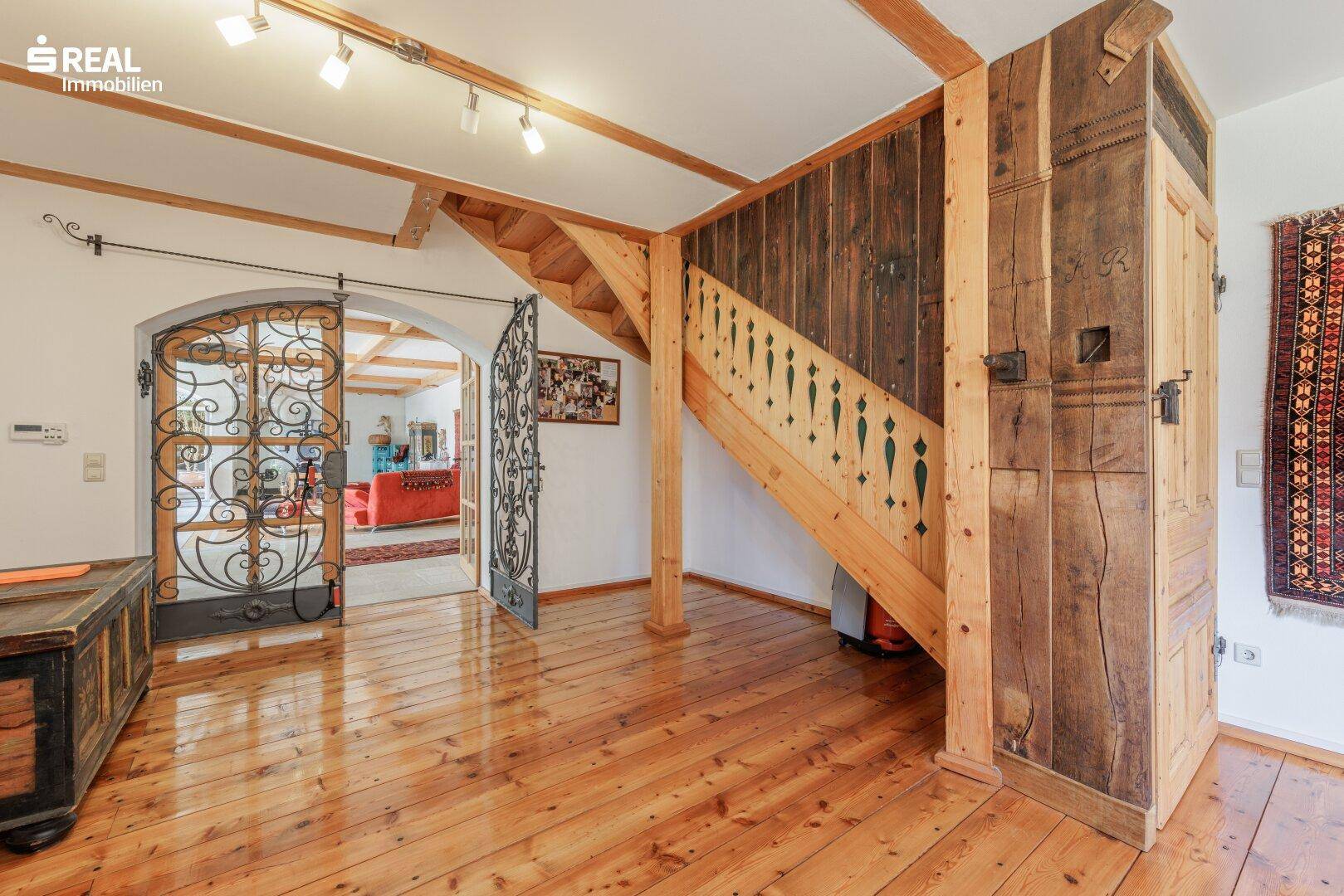 Rustikaler Eingangsbereich mit Holzboden, Holztreppe und schmiedeeisernem Tor zu den Wohnräumen.