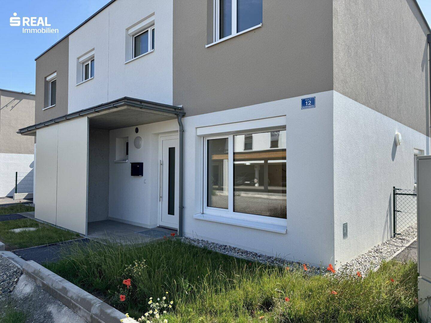 Eingangsbereich eines modernen Reihenhauses mit kleiner Grünfläche und Hausnummer.
