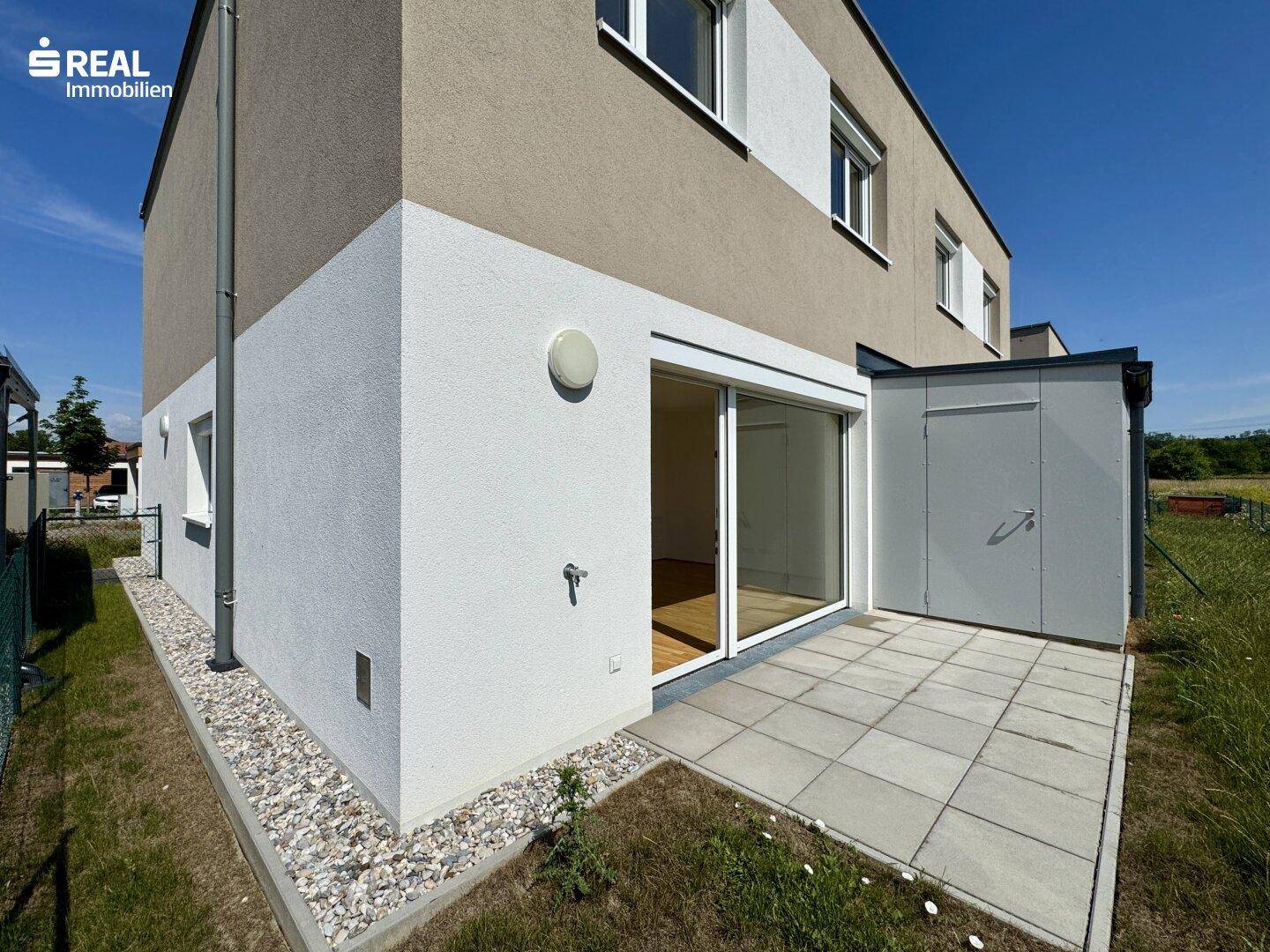Rückseite des Hauses mit einer gepflasterten Terrasse und Zugang zum Gartenbereich.