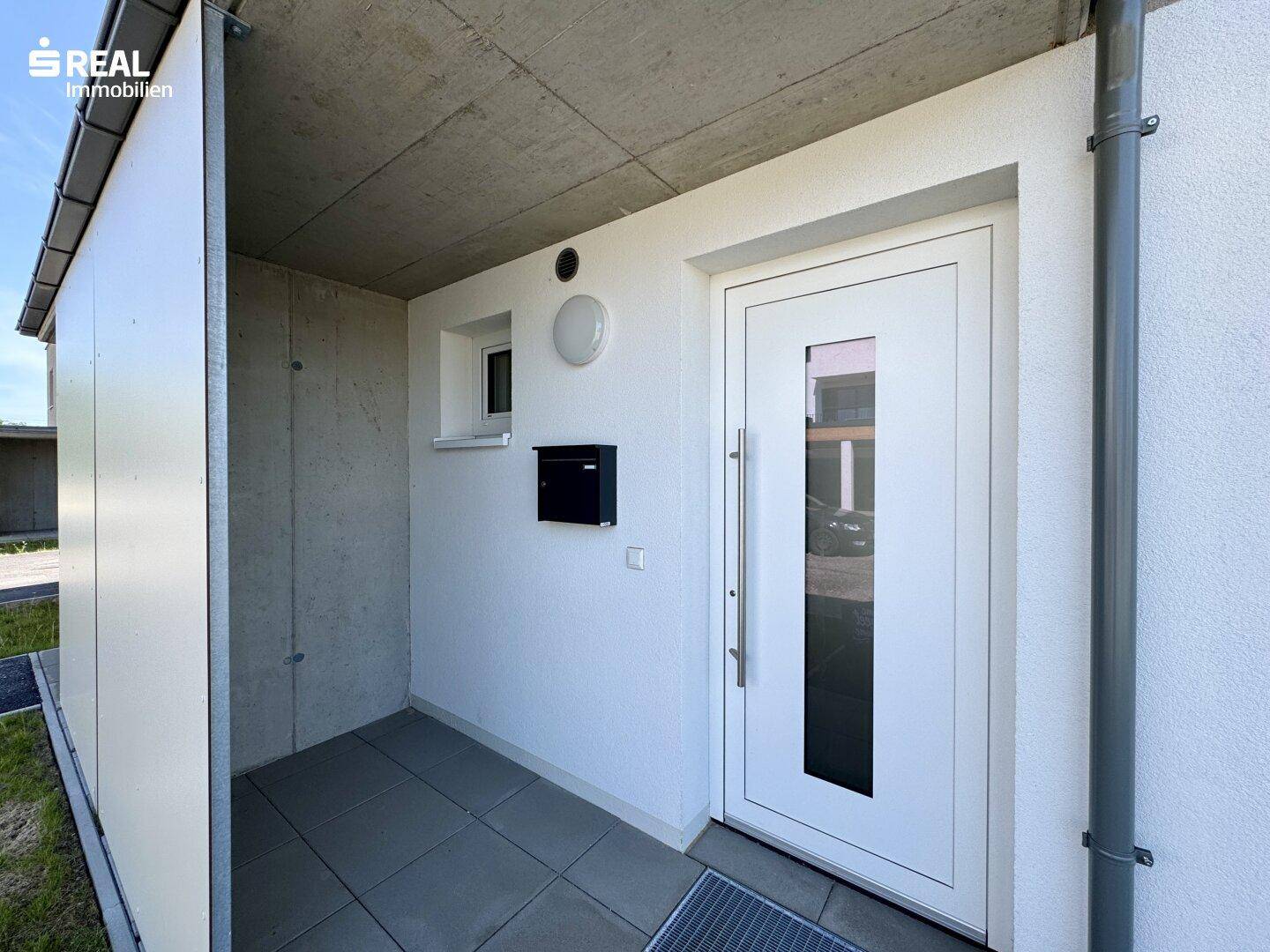 Heller Eingangsbereich mit moderner Haustür und Briefkasten unter einem Vordach.