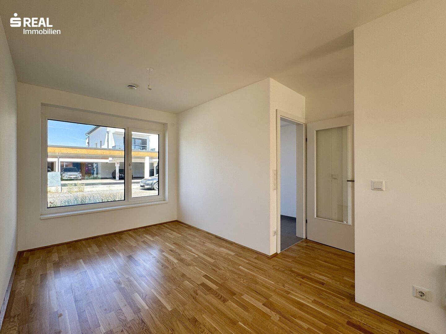 Helles Zimmer mit Parkettboden und großem Fenster, ideal als Arbeits- oder Gästezimmer.