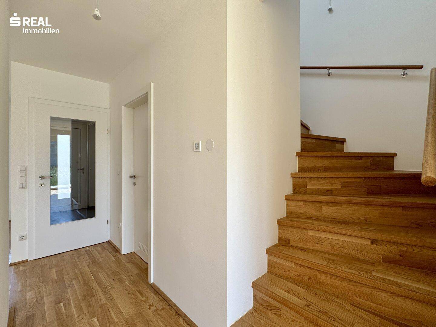 Heller Flur mit Holztreppe, die in das obere Stockwerk führt, und Parkettboden.